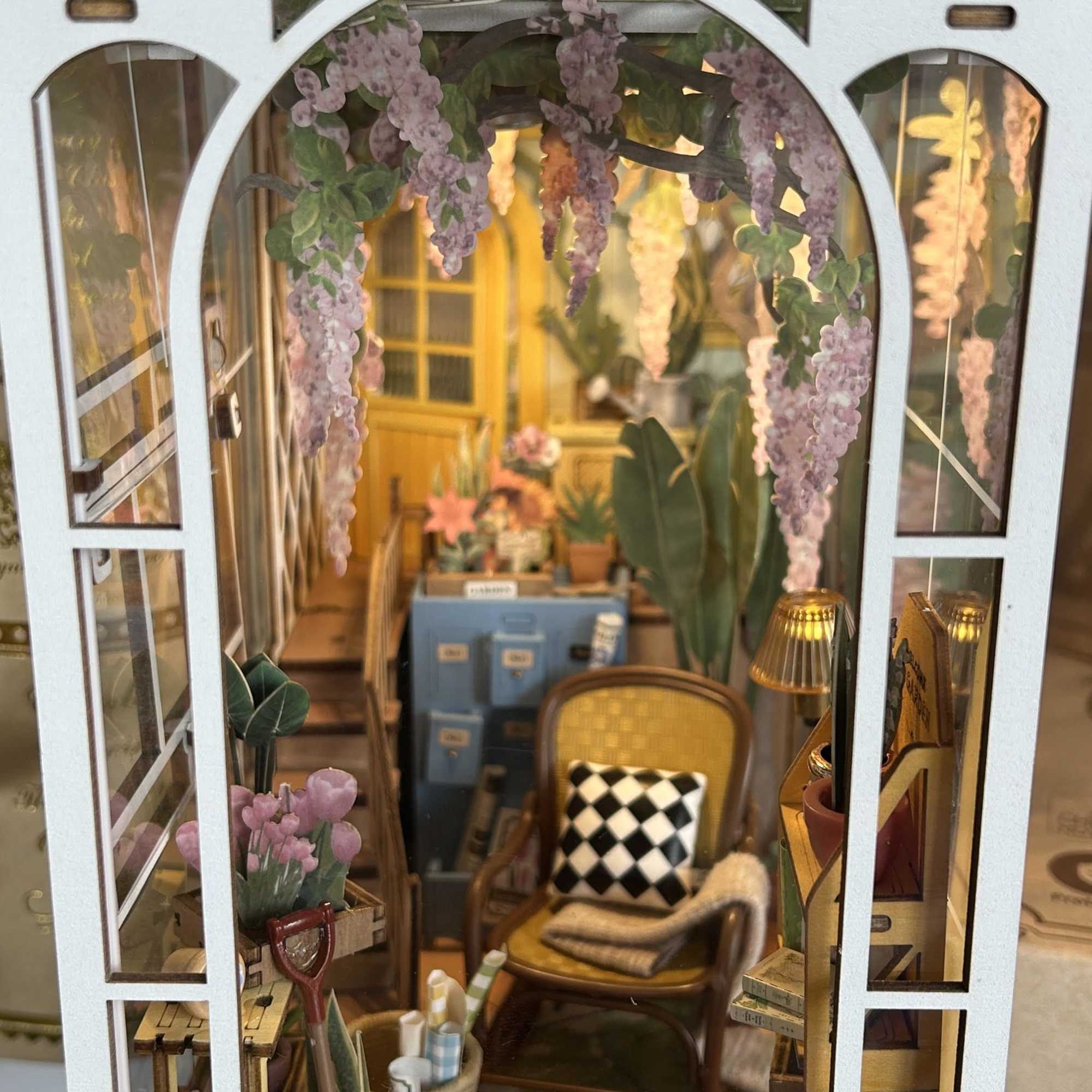Miniature greenhouse display with hanging purple flowers and small potted plants