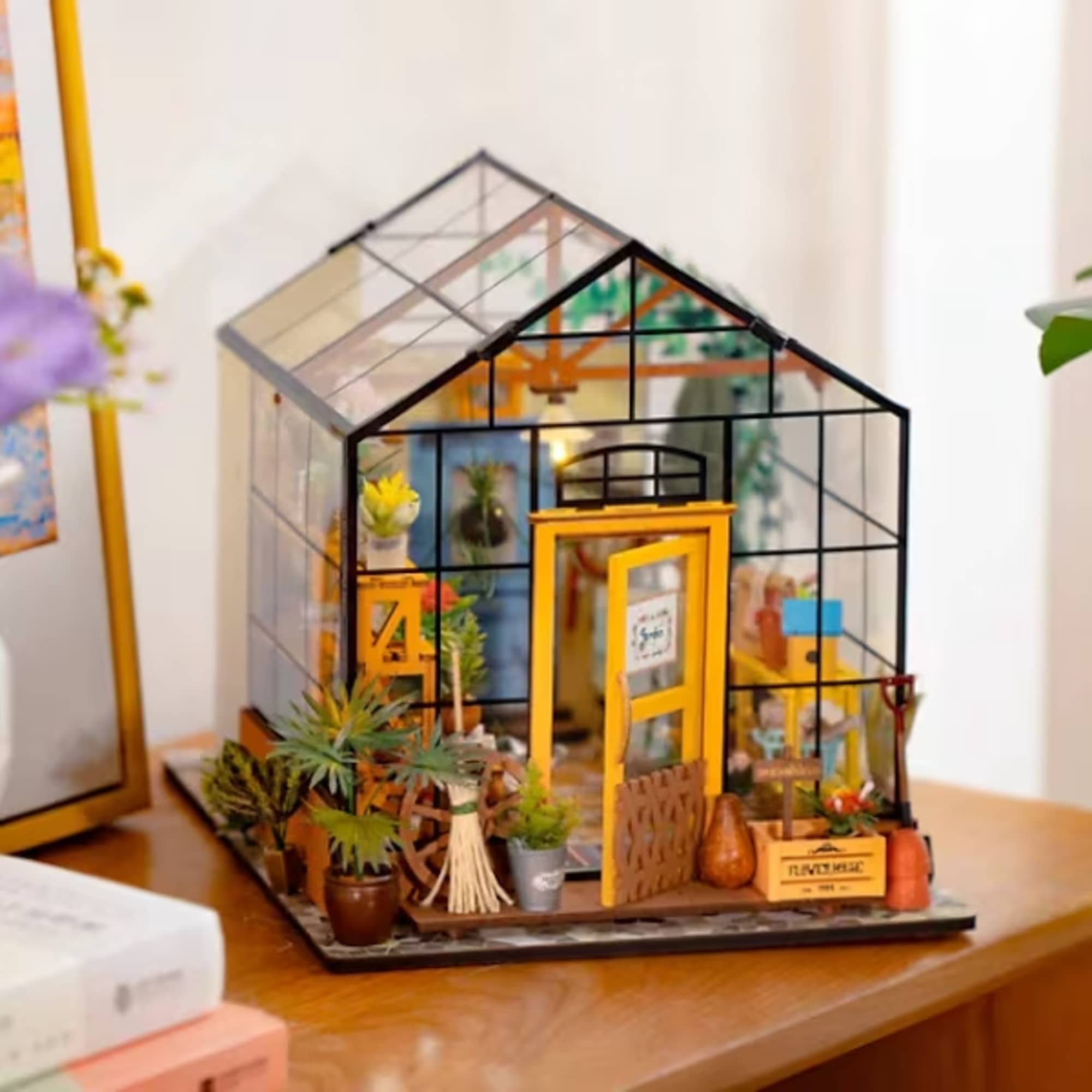 Miniature greenhouse display with tiny potted plants and a yellow door