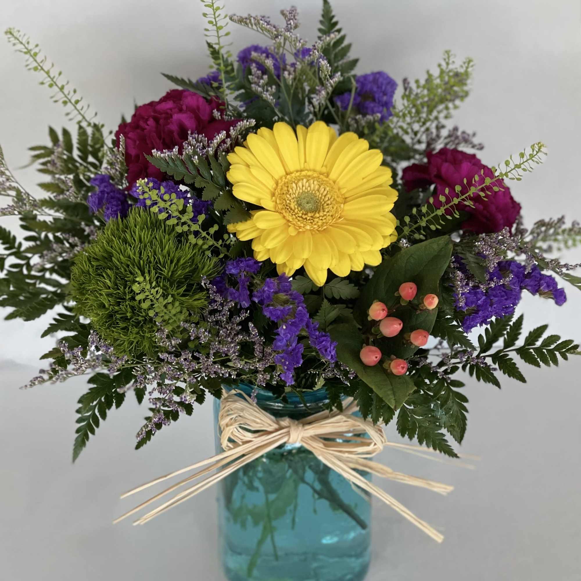 Mixed bouquet with a yellow gerbera daisy in a blue glass vase