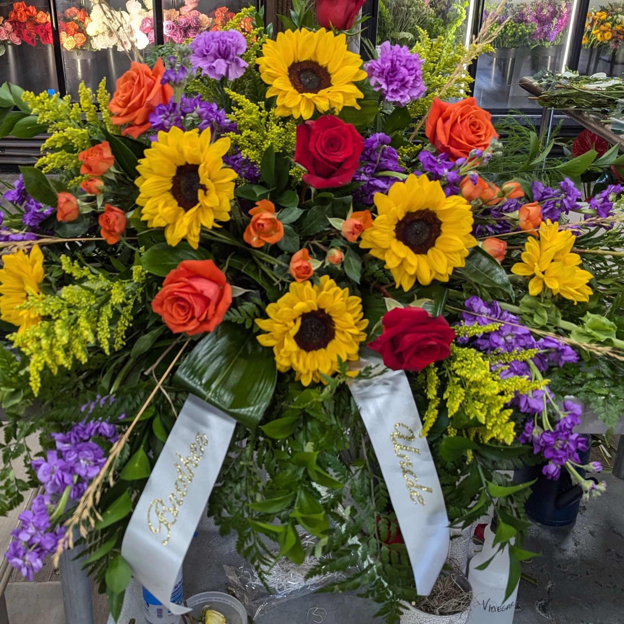 Casket spray includes Red and Orange Roses, Sunflowers, Carnations, Stock, Bells of
