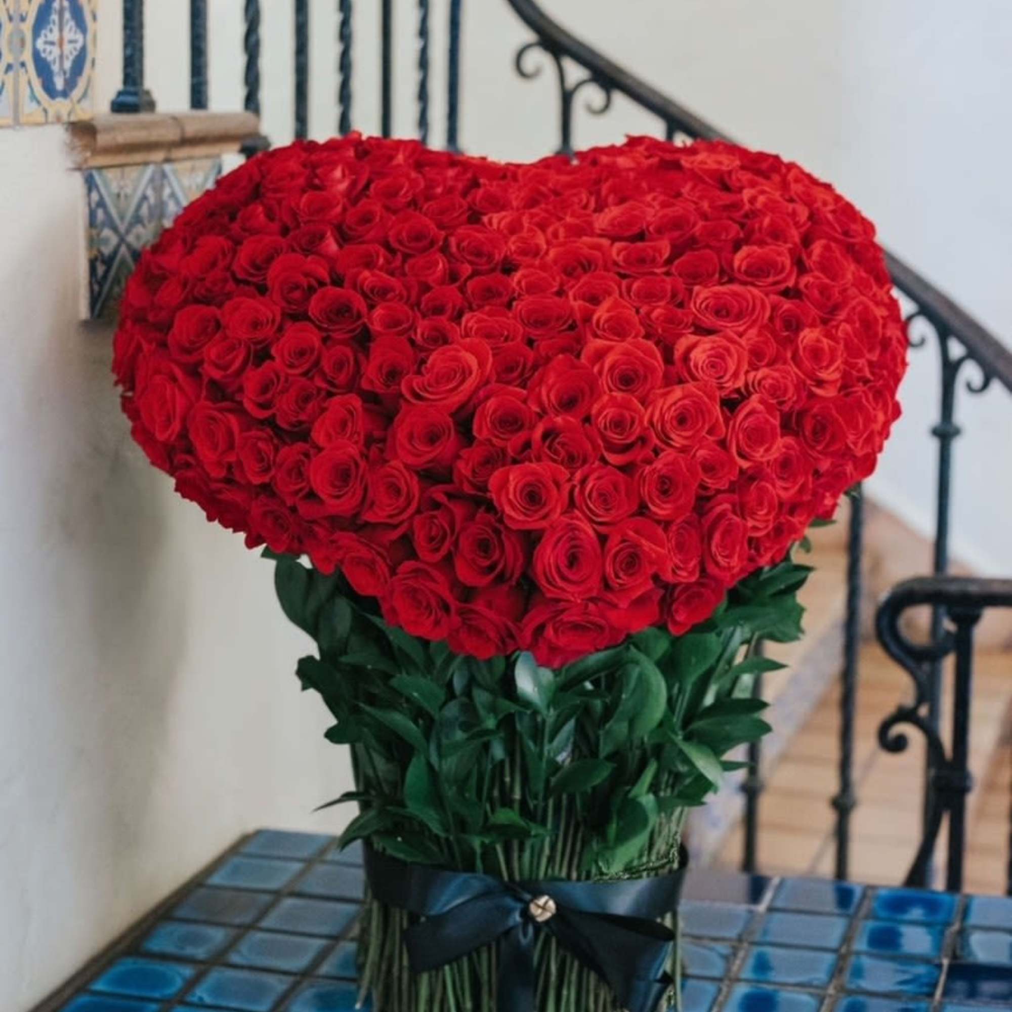 Large heart-shaped bouquet of red roses with a dark ribbon wrap