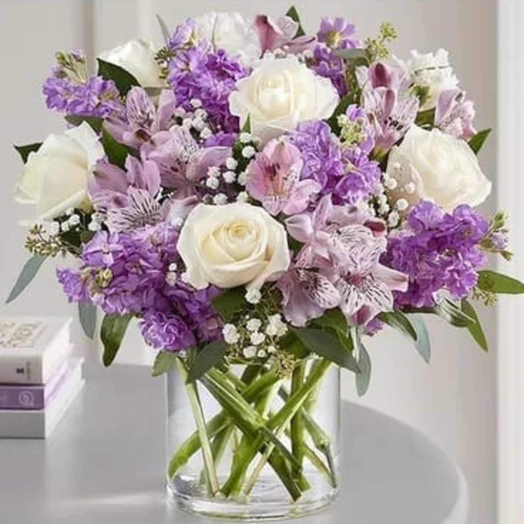 Bouquet of white roses and purple flowers in a clear glass vase