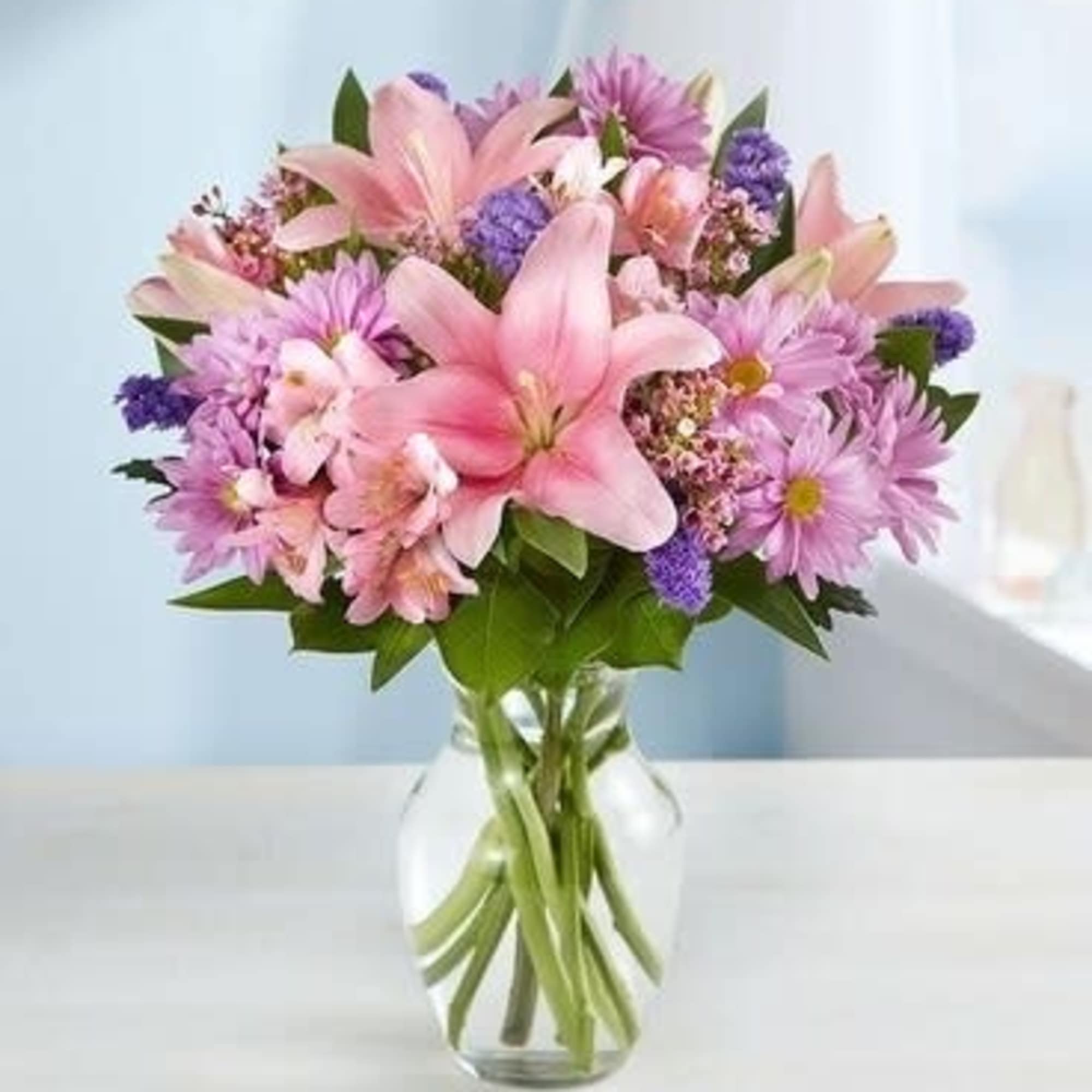 Pink lilies and purple daisies in a clear glass vase