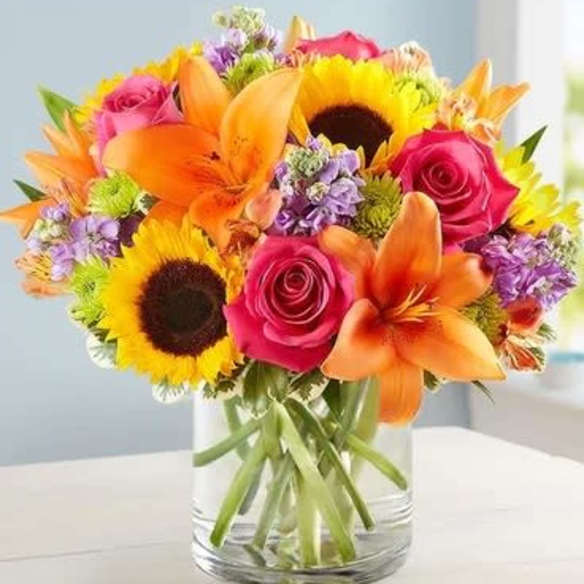Bright mixed bouquet with sunflowers, roses, and lilies in a glass vase