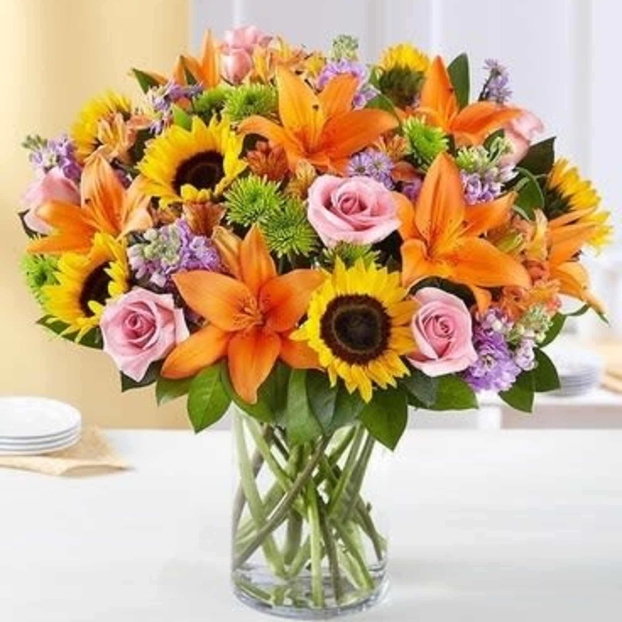 Bouquet of sunflowers, orange lilies, and pink roses in a glass vase