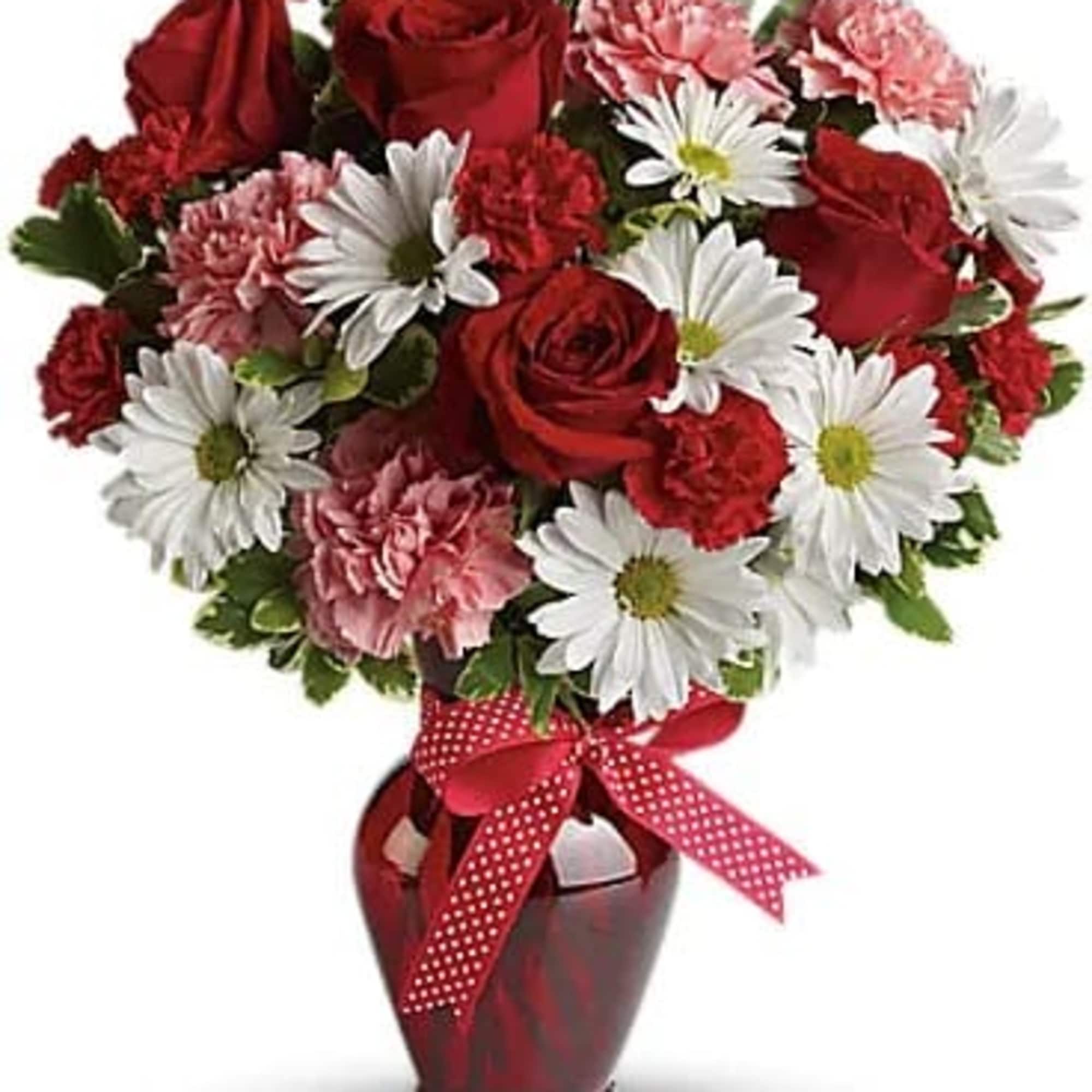 Red roses, pink carnations, and white daisies in a red vase with a ribbon