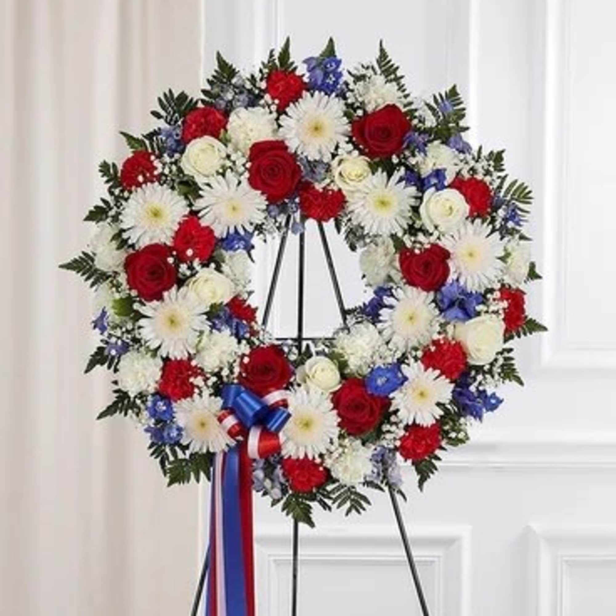 Circular wreath of red, white, and blue flowers on a stand with ribbon