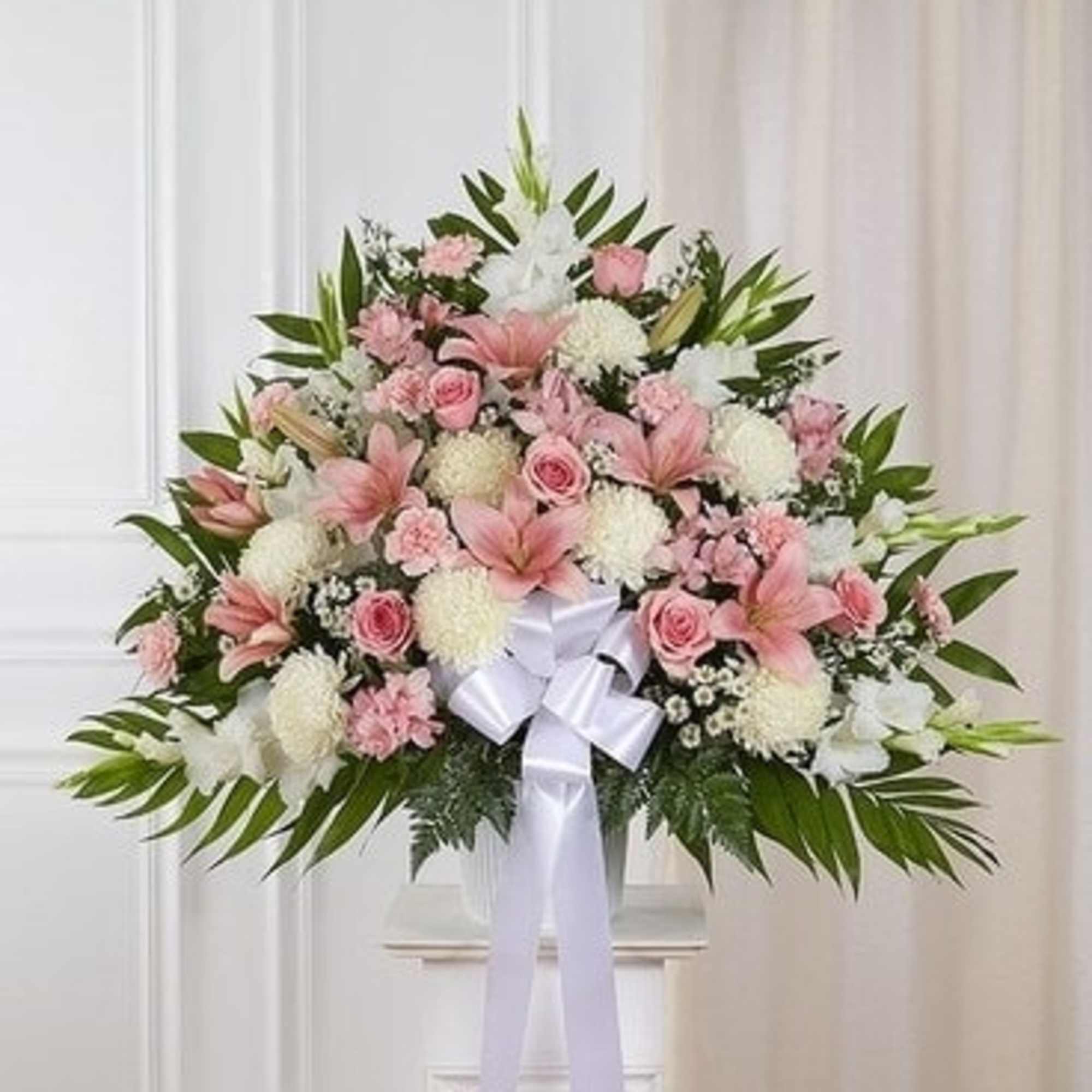 Pink and white funeral spray with lilies, roses, and a white ribbon