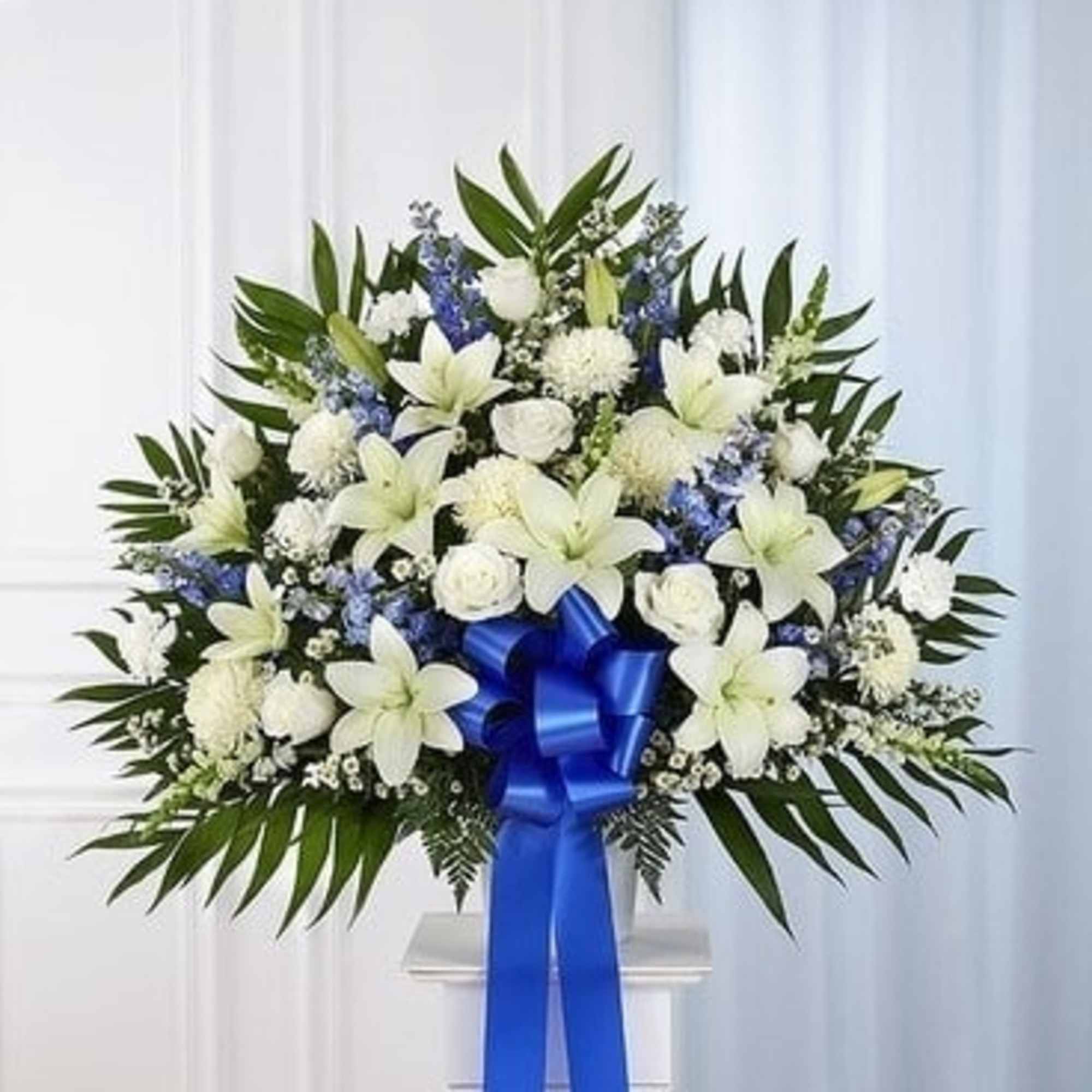 White lilies and roses in a standing spray with a blue ribbon