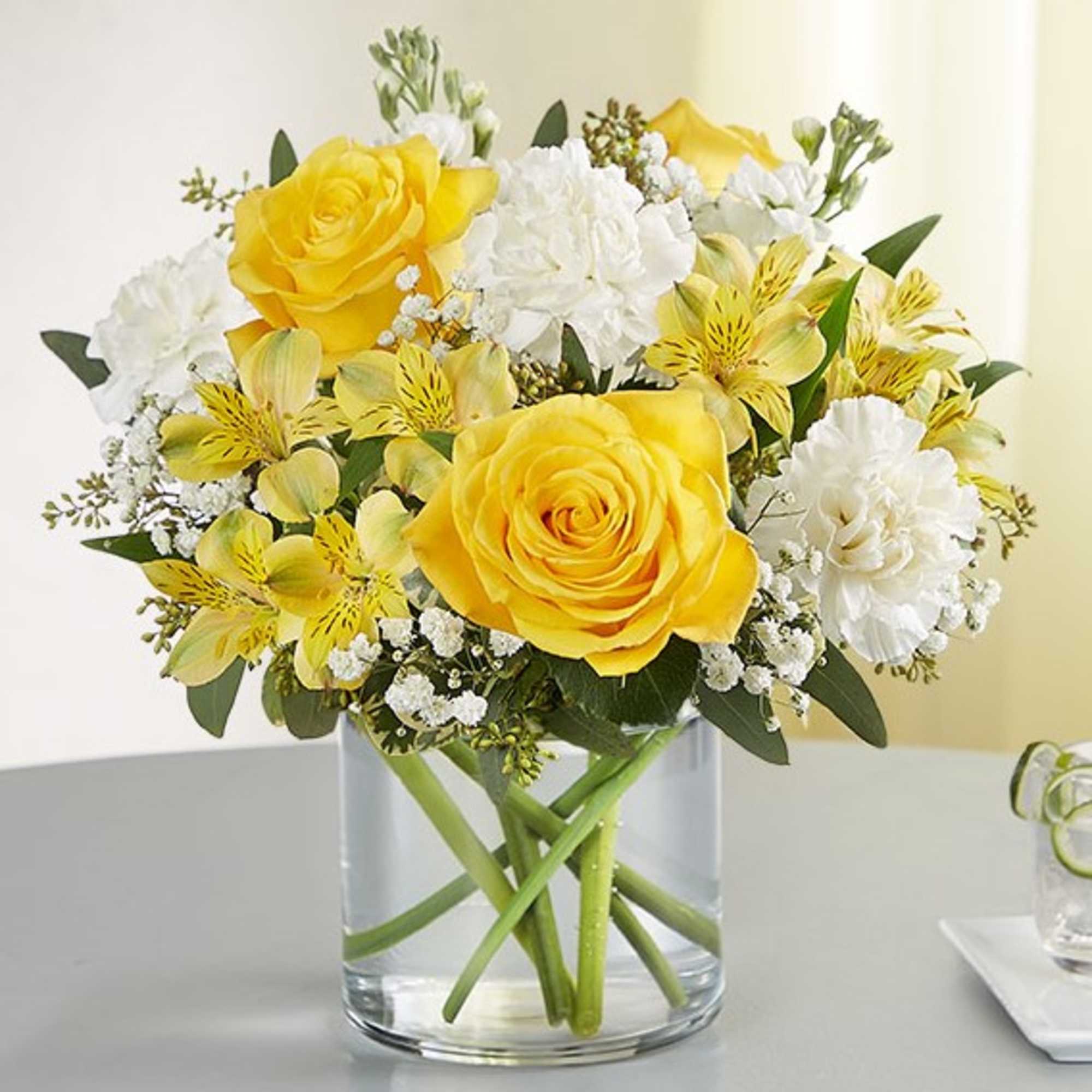 Yellow roses and white flowers arranged in a clear glass vase