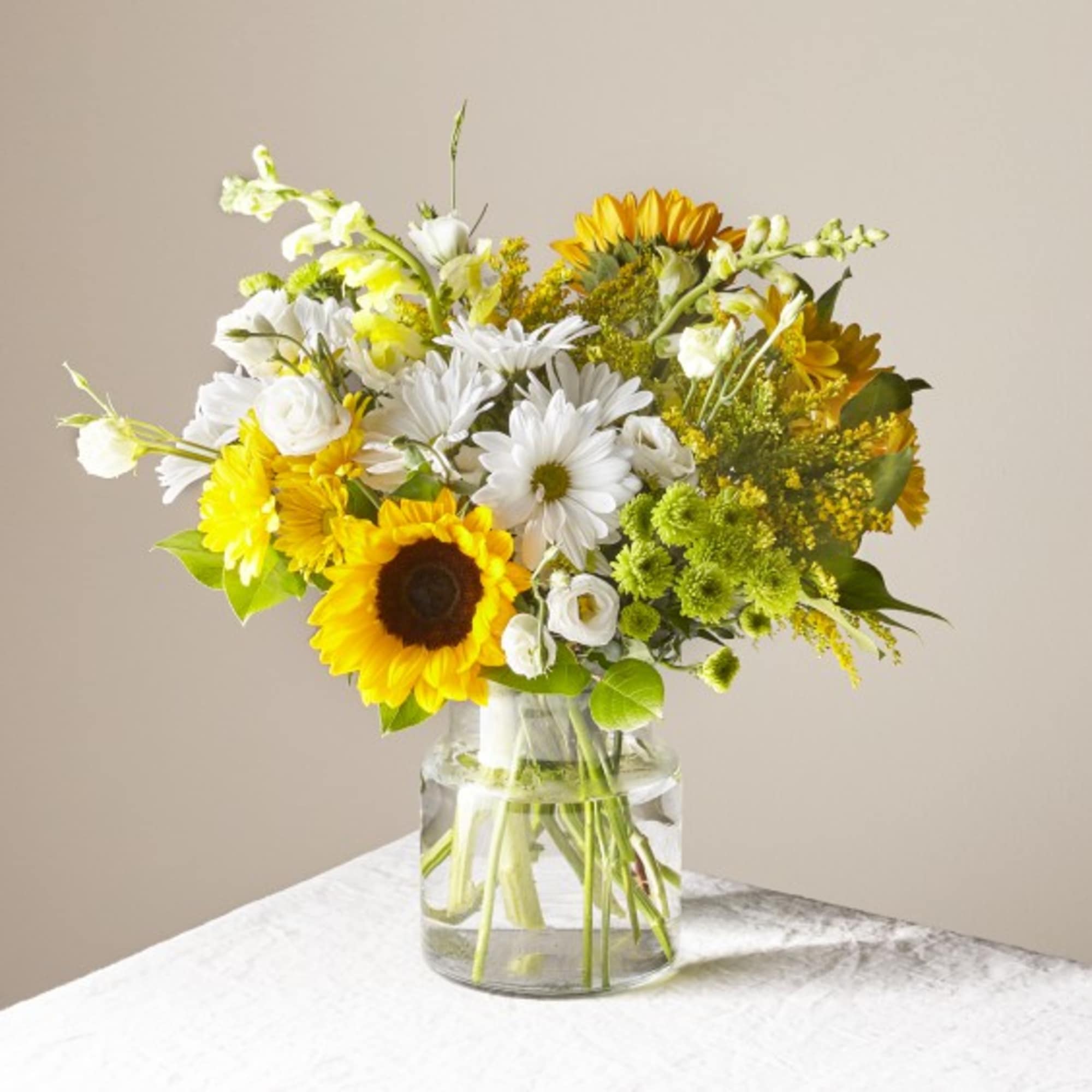 Bouquet of sunflowers, white daisies, and yellow flowers in a glass vase