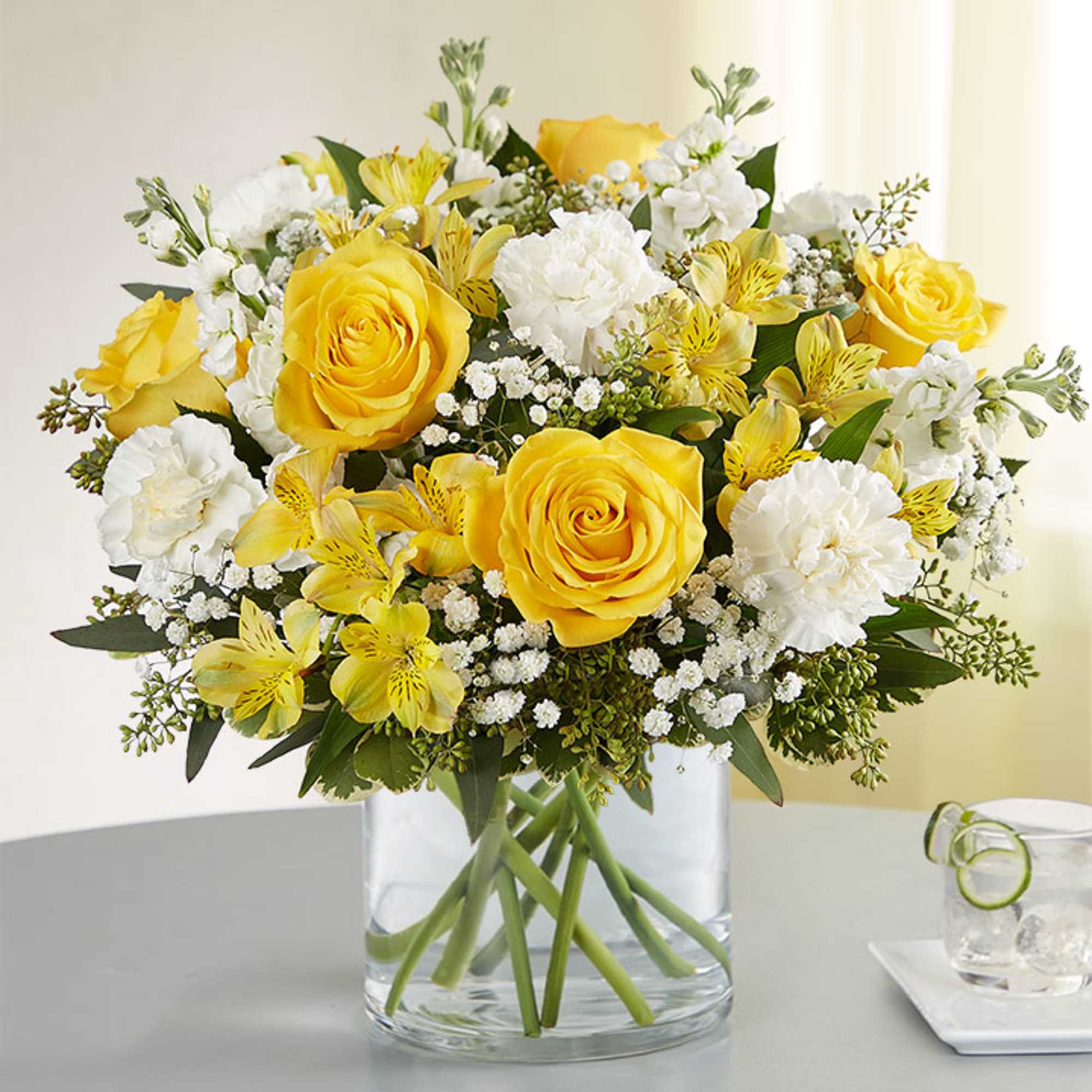 Yellow roses and white flowers in a clear glass vase