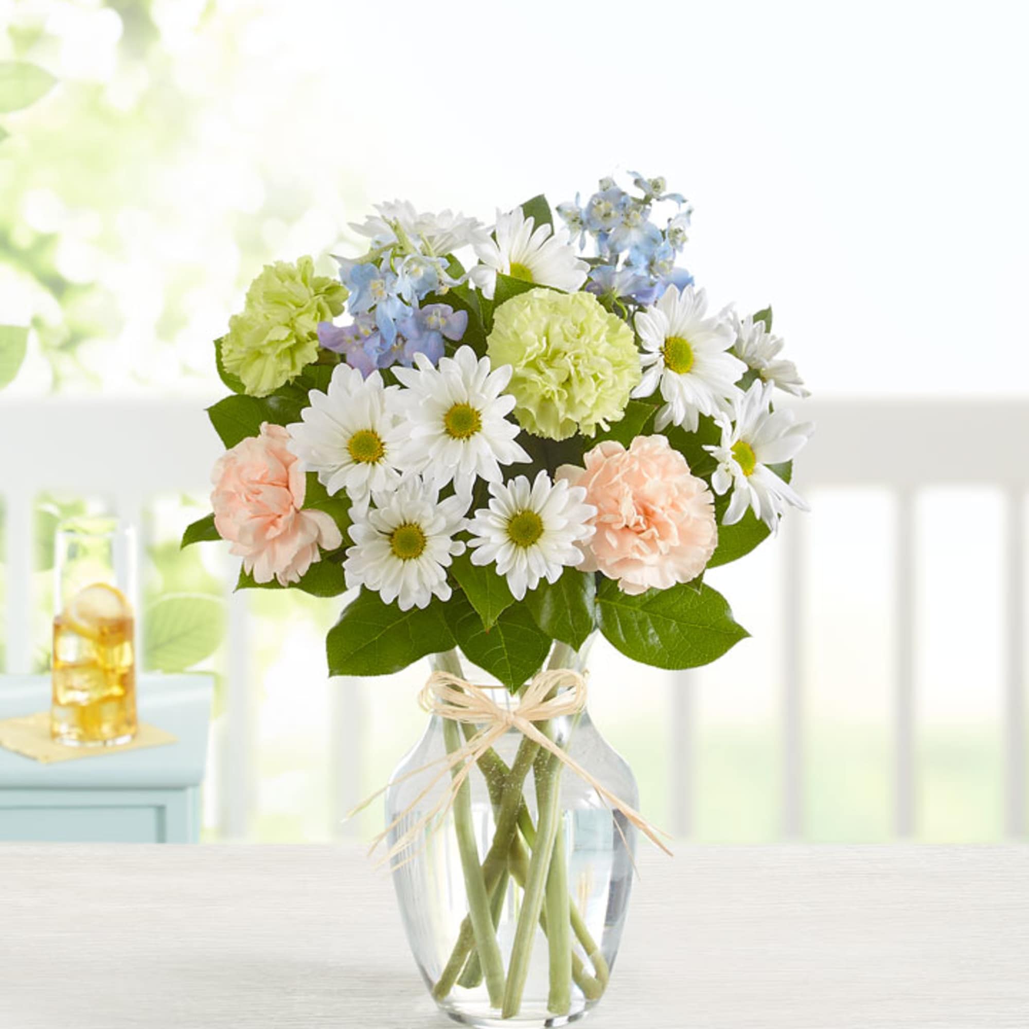 Bouquet of white daisies, pale carnations, and blue flowers in a glass vase