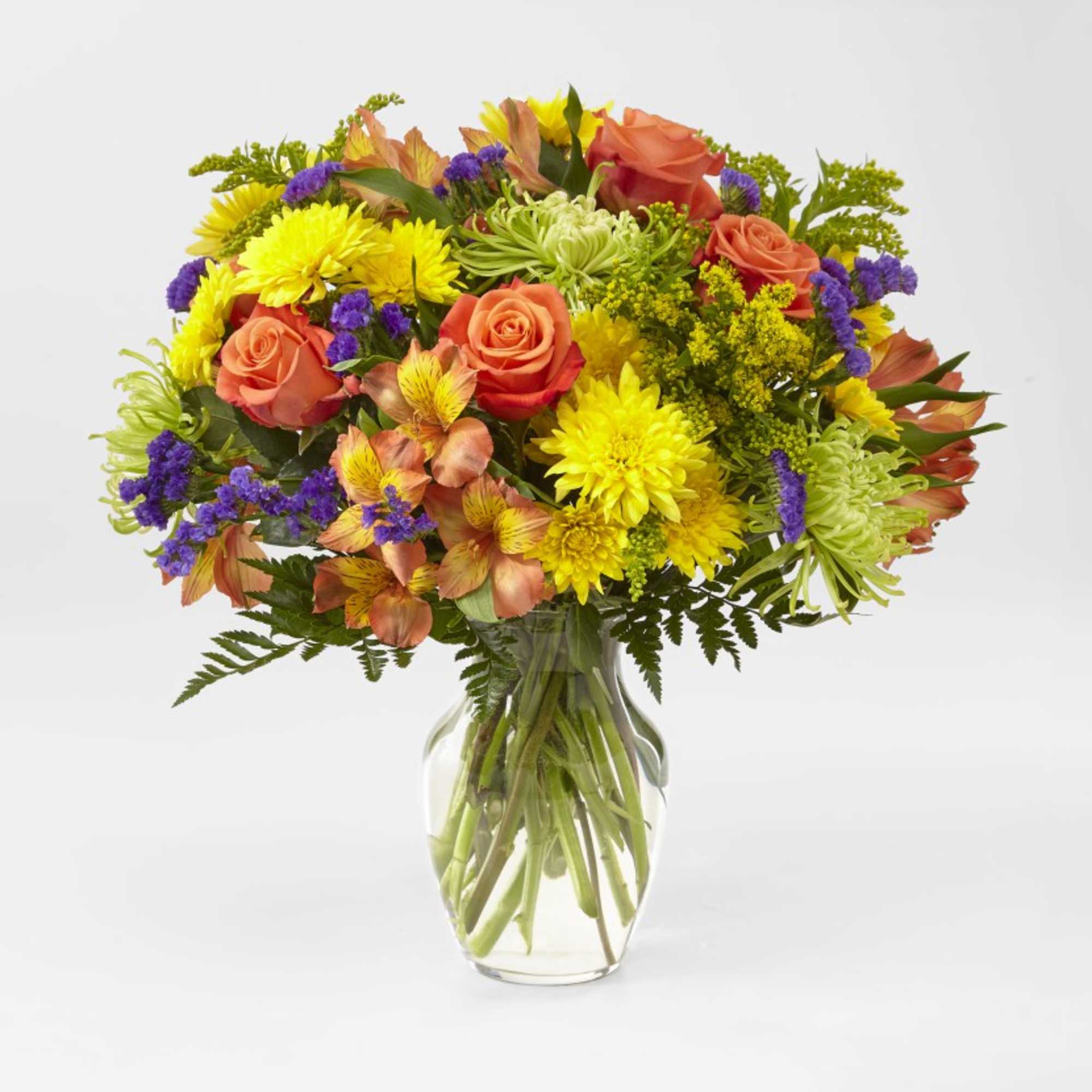 Mixed bouquet of orange roses, yellow mums, and purple filler in a glass vase