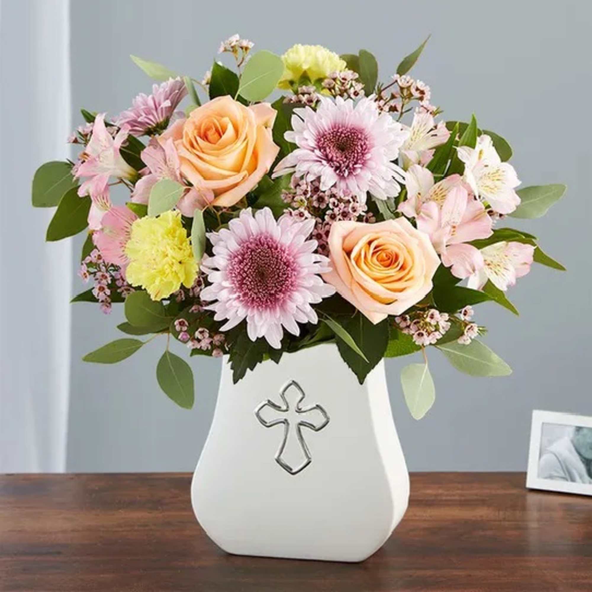 Pastel flower arrangement in a white vase with a cross emblem