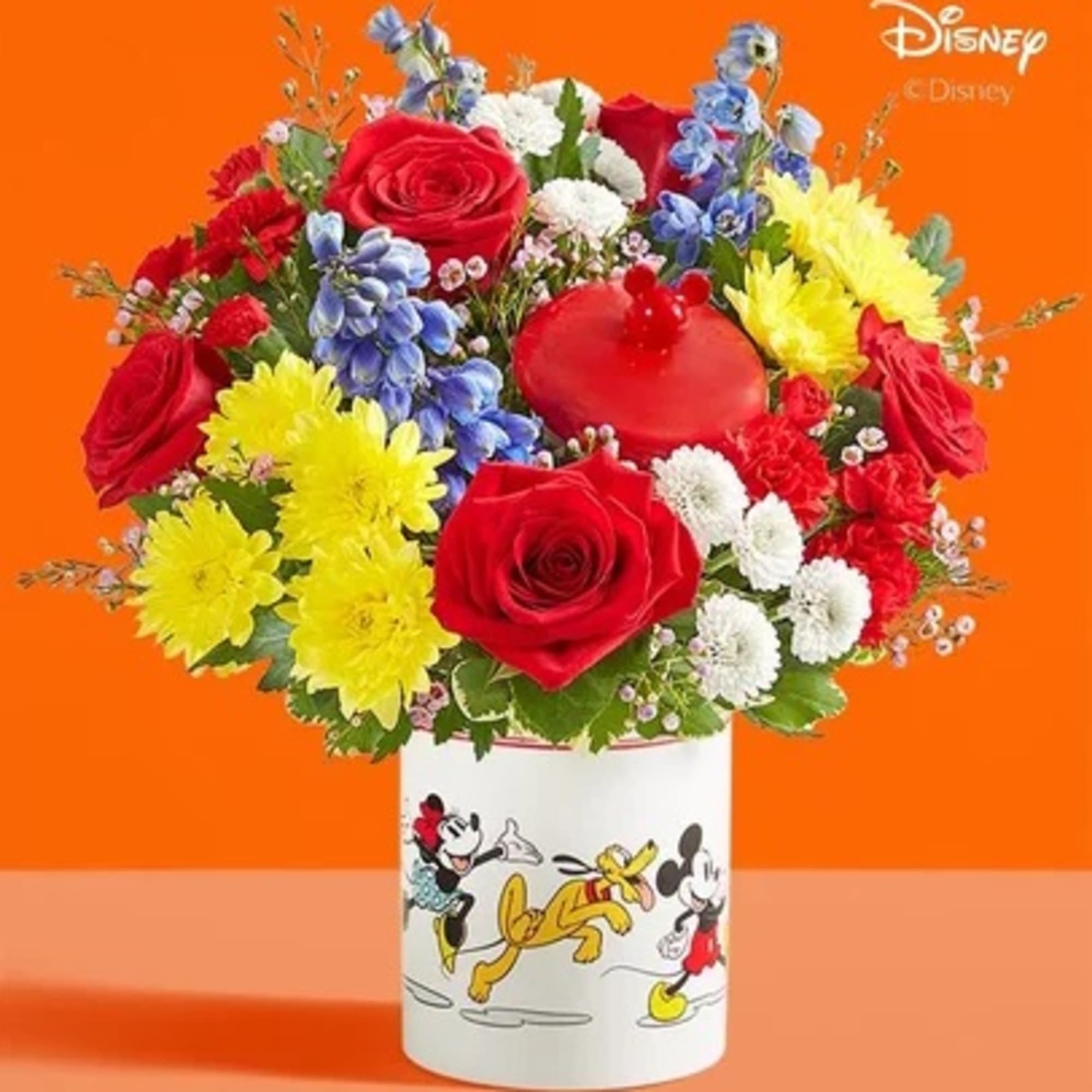 Bouquet of red roses, yellow daisies, and blue flowers in a Mickey Mouse vase