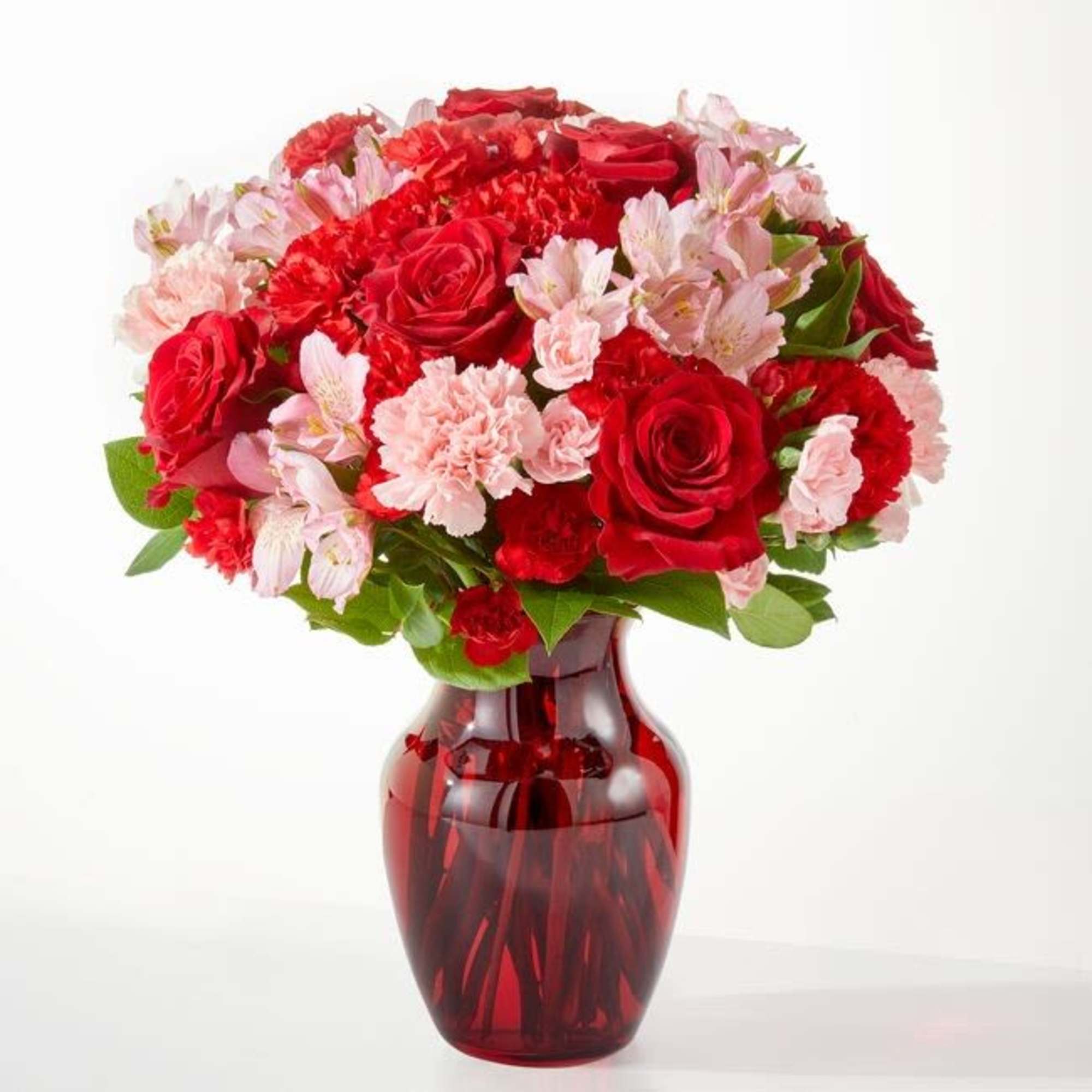 Red roses and pink flowers arranged in a red glass vase