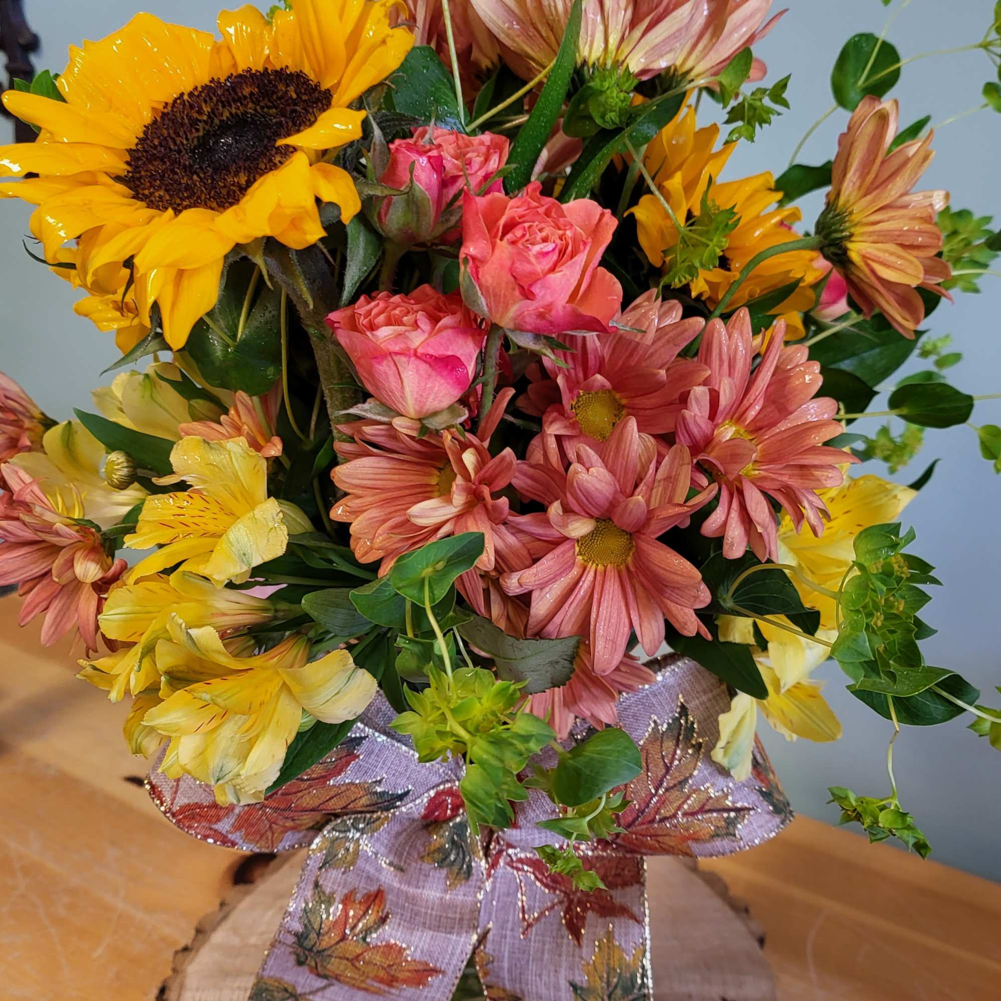 Bouquet of sunflowers, pink roses, and daisies in a glass vase