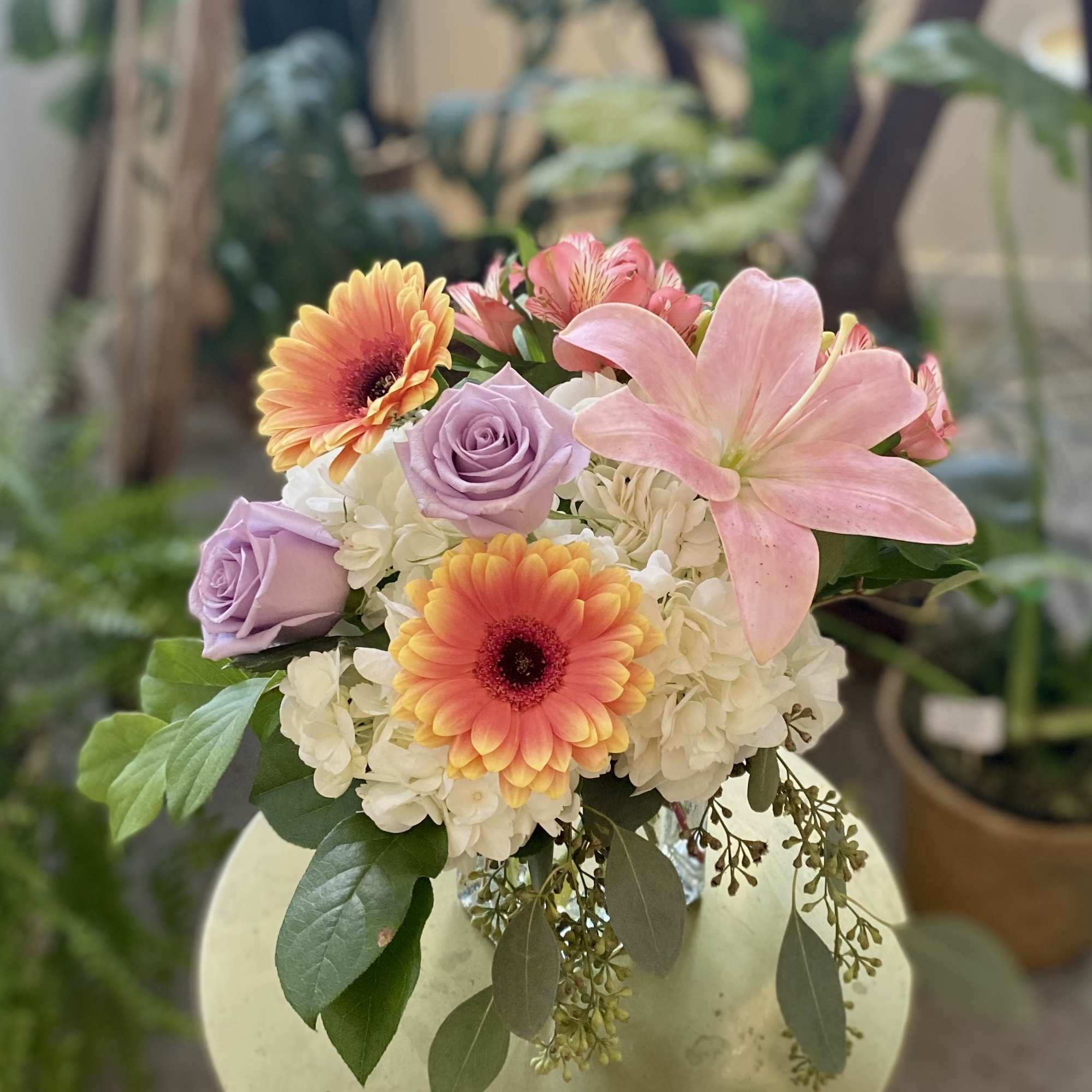 Mixed bouquet with pink lily, orange gerbera daisies, lavender roses and white blooms in a clear glass vase