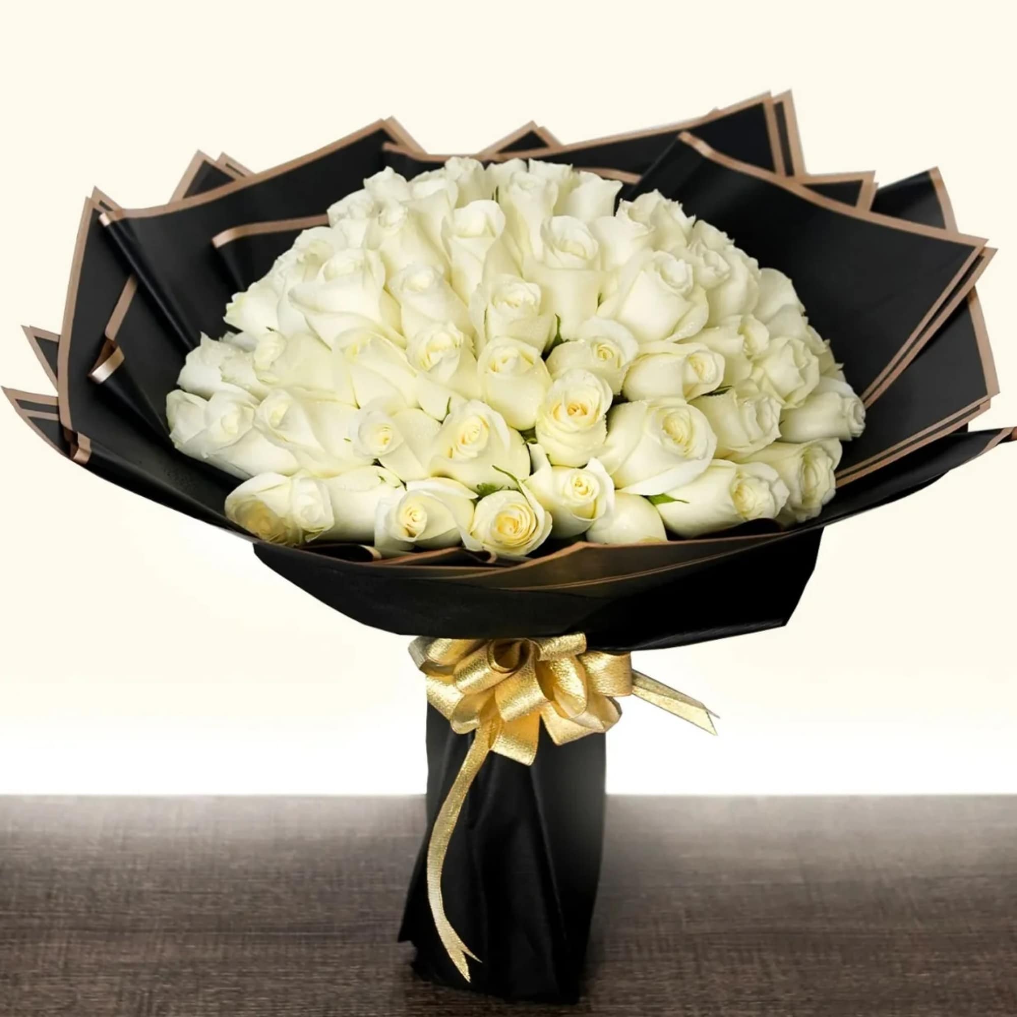Bouquet of white roses wrapped in black paper with a gold ribbon