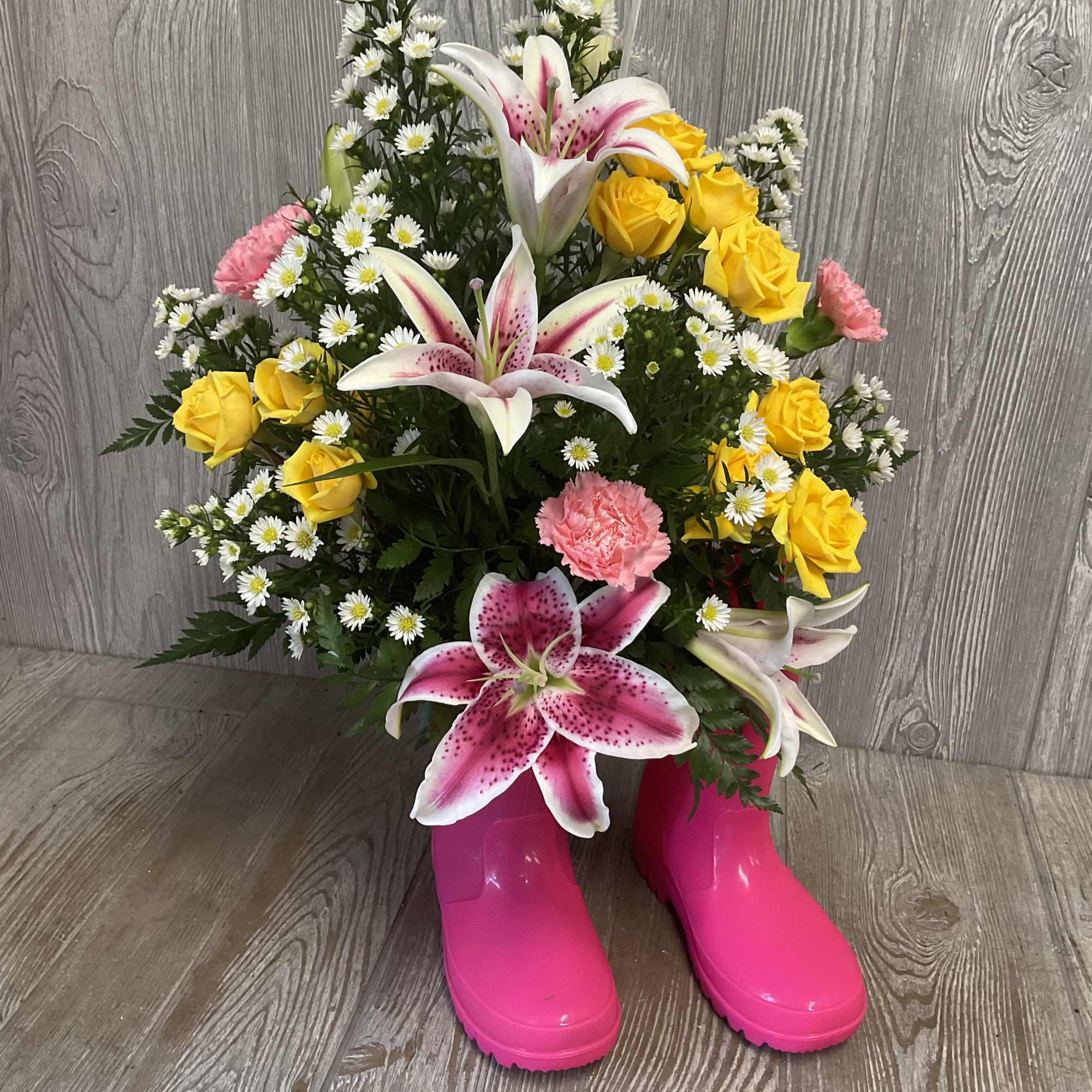 Bouquet of pink lilies, yellow roses, and white daisies in bright pink boots
