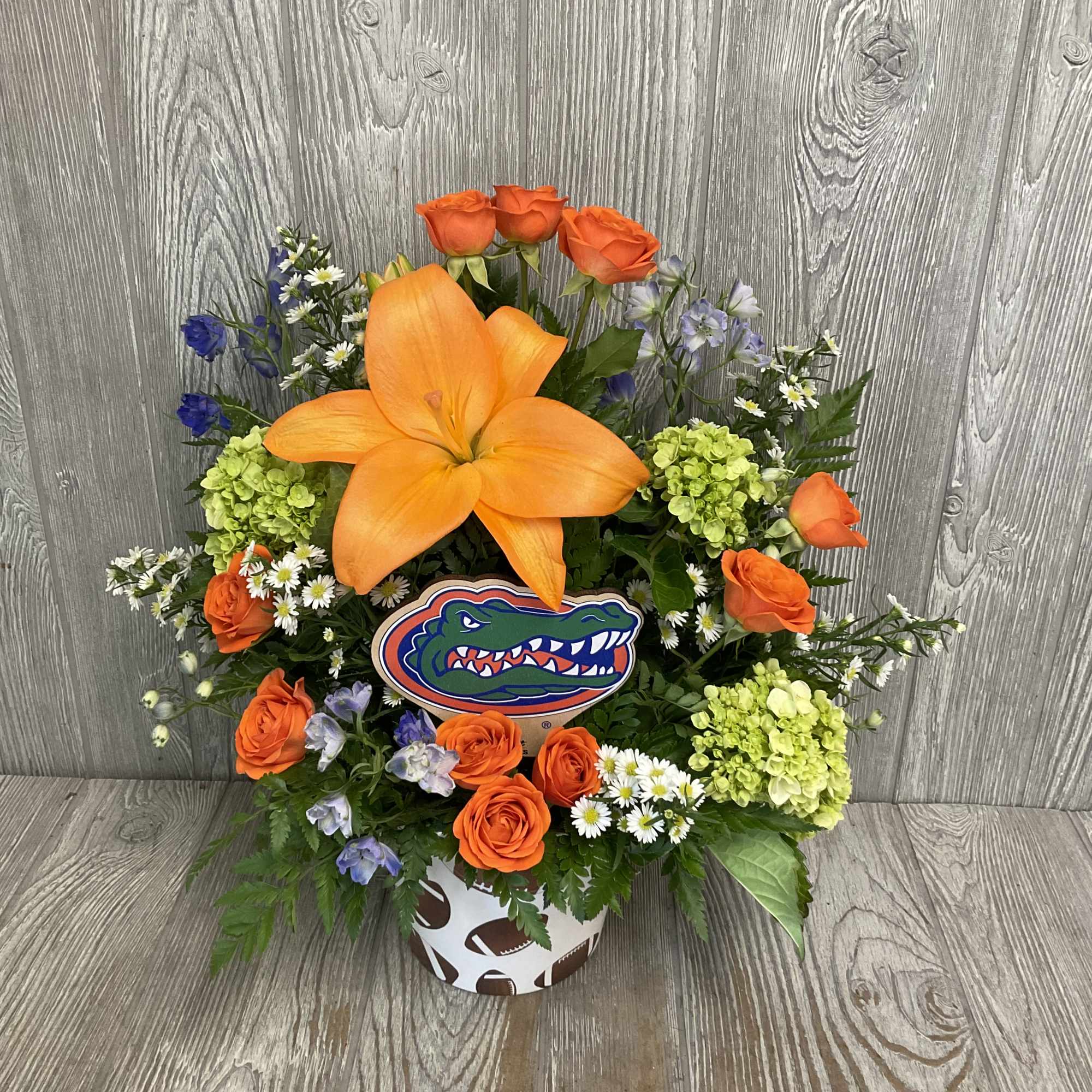Football-themed flower arrangement with orange roses and a large orange lily in a sports container
