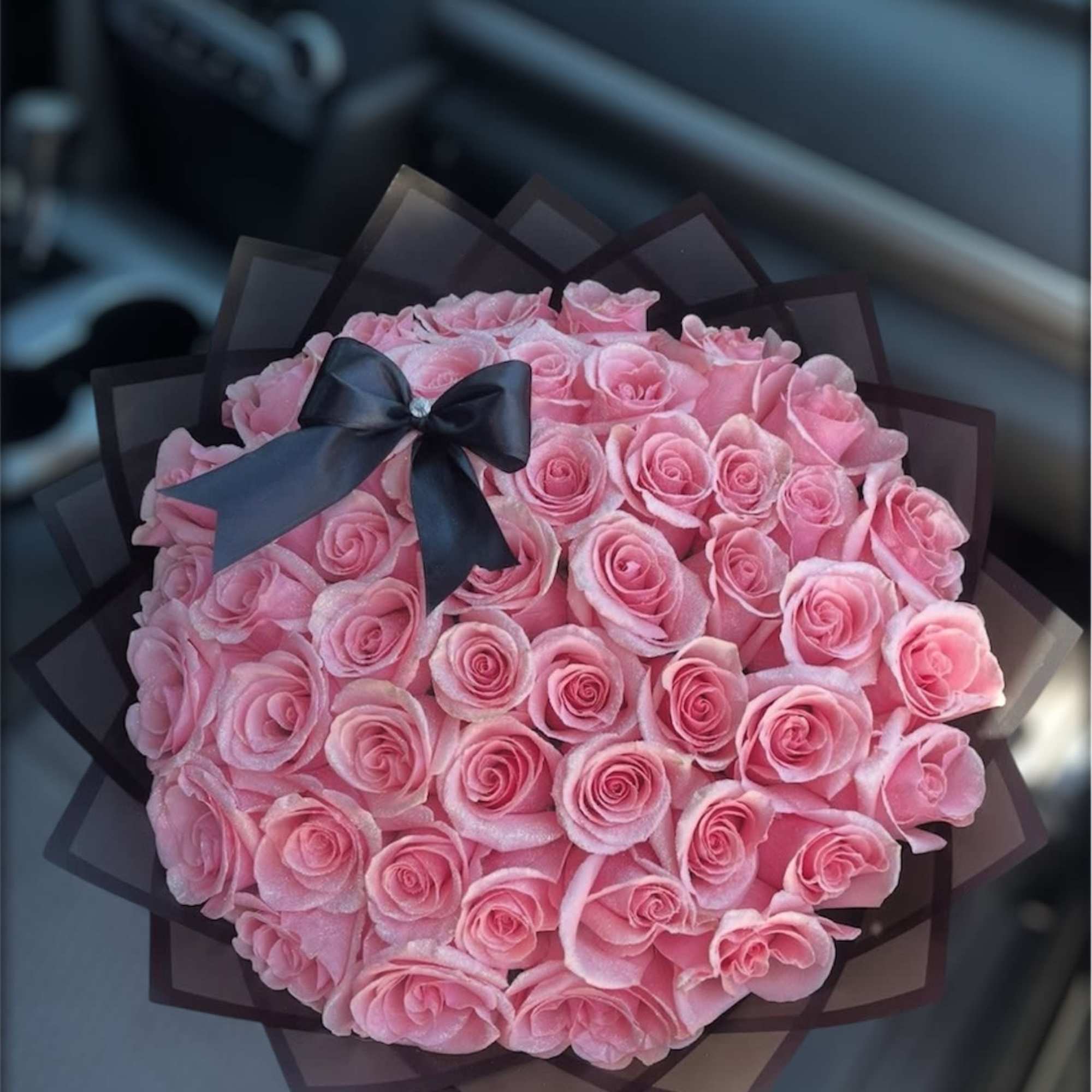 Round bouquet of pink roses wrapped in dark paper with a black ribbon