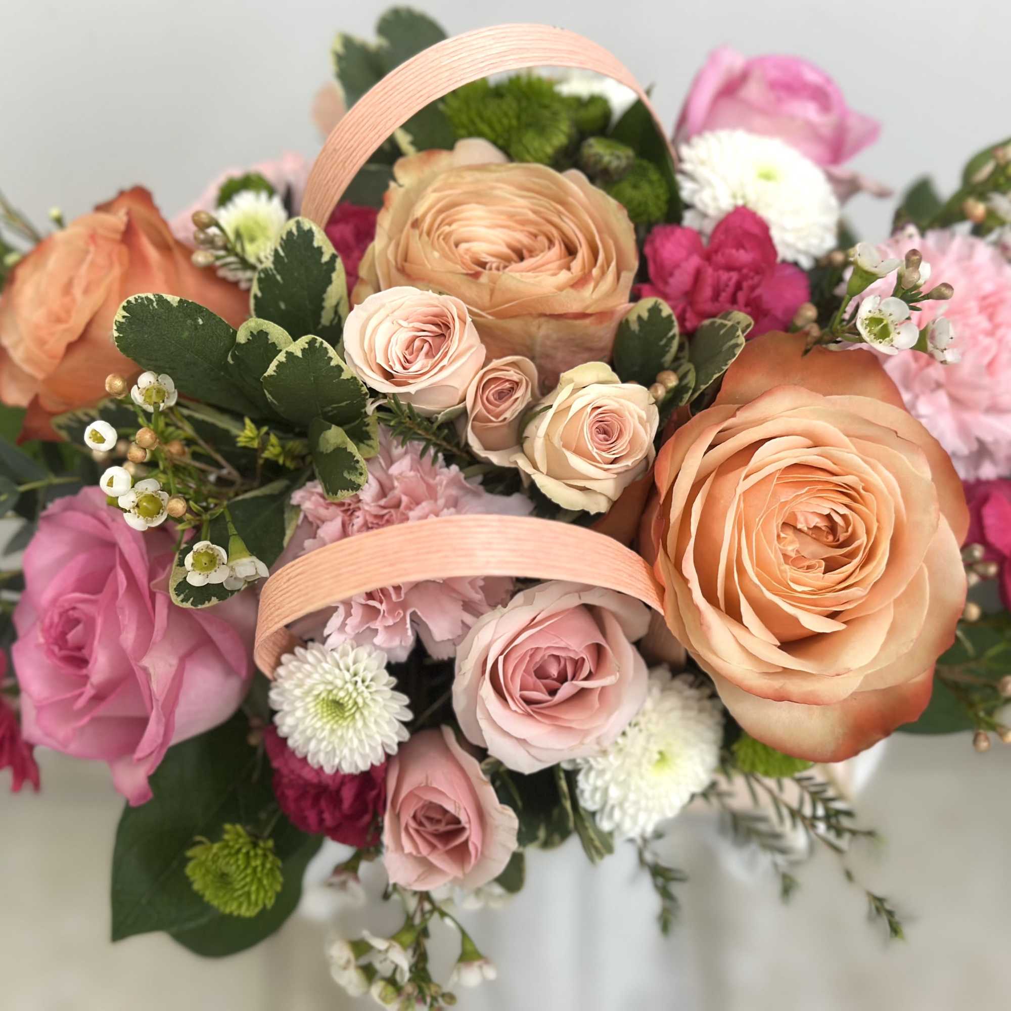Rounded bouquet of peach and pink roses, carnations, and white mums with decorative ribbon loops.
