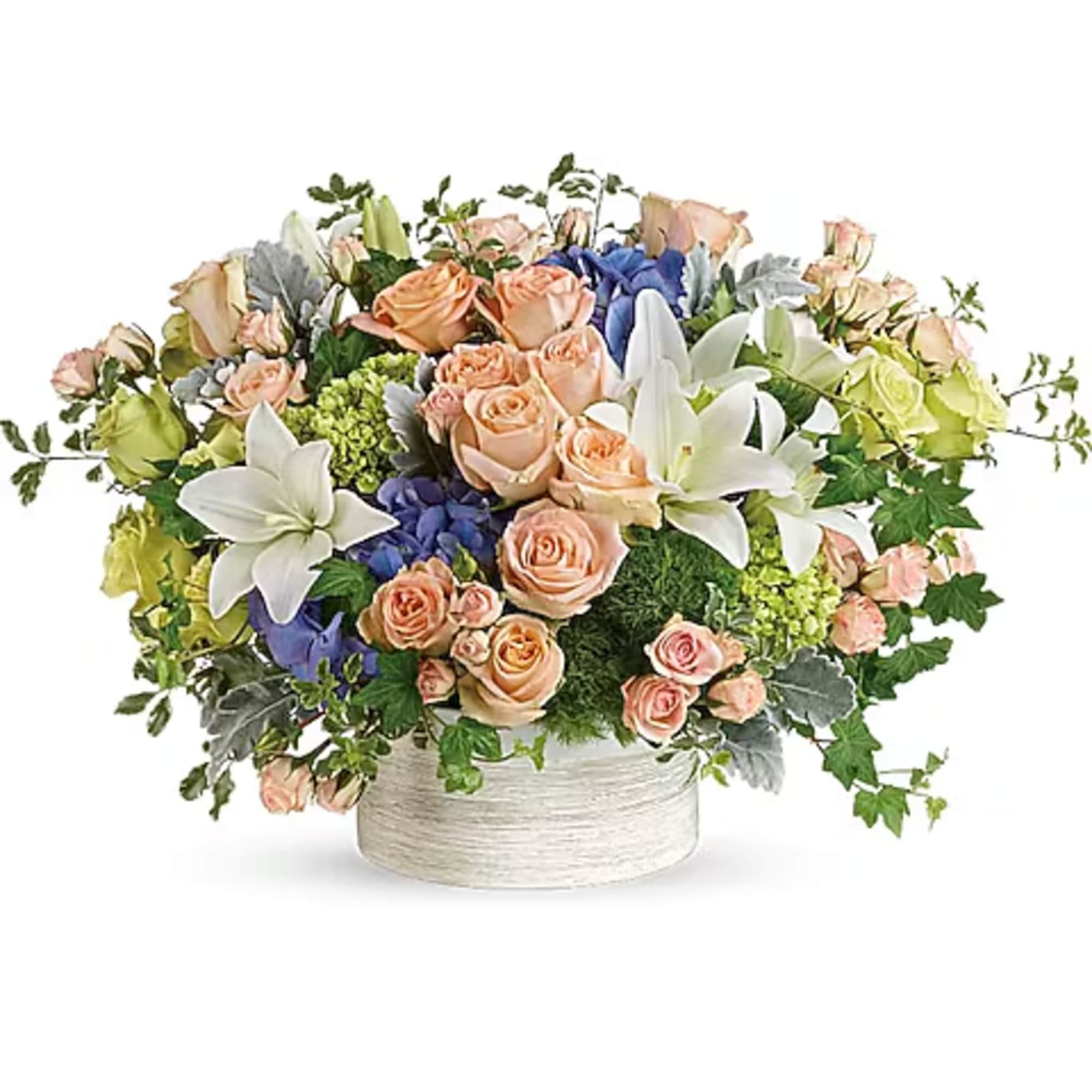 Mixed bouquet of peach roses, white lilies, and blue flowers in a white container
