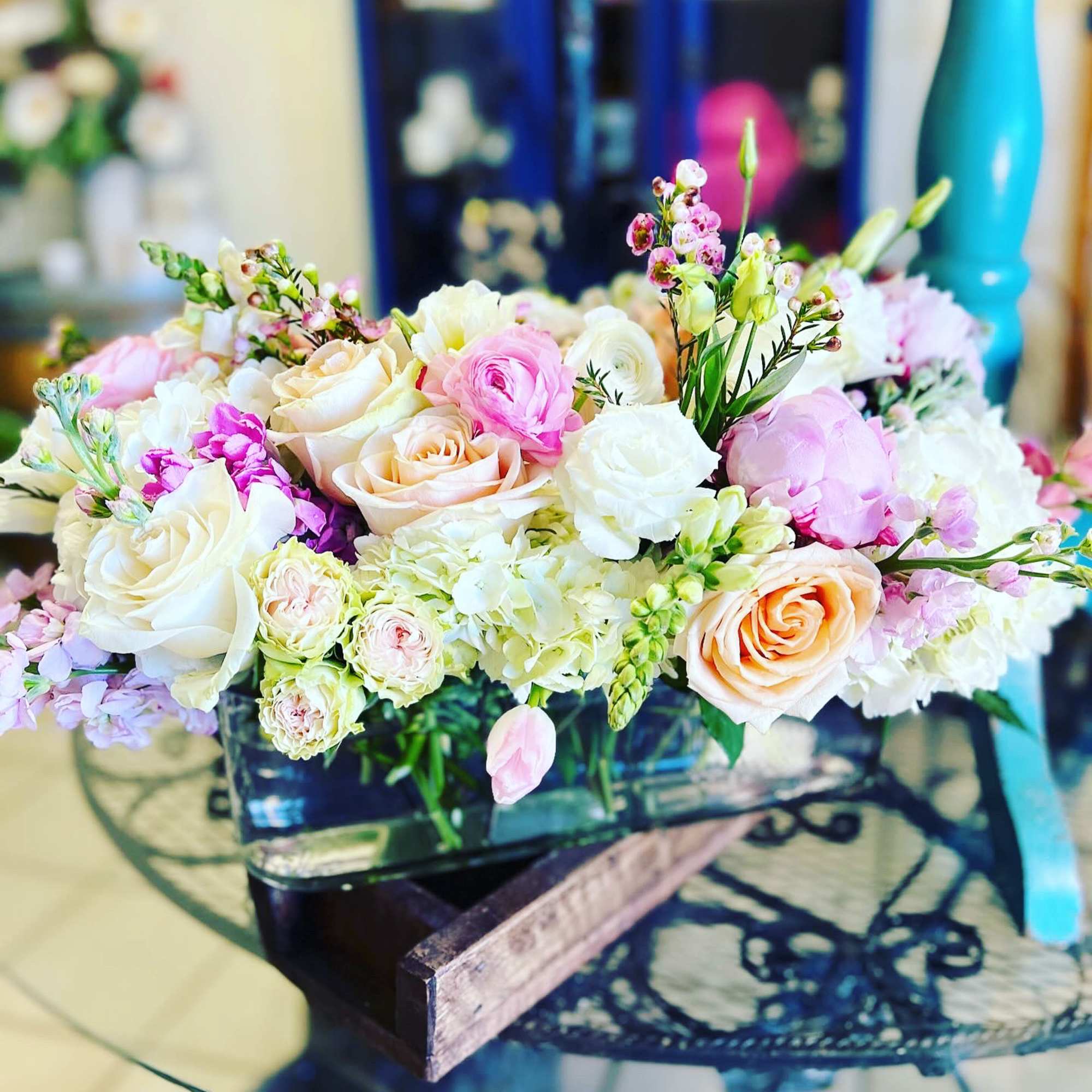 Pastel bouquet of roses, ranunculus, and small pink blooms in a low container