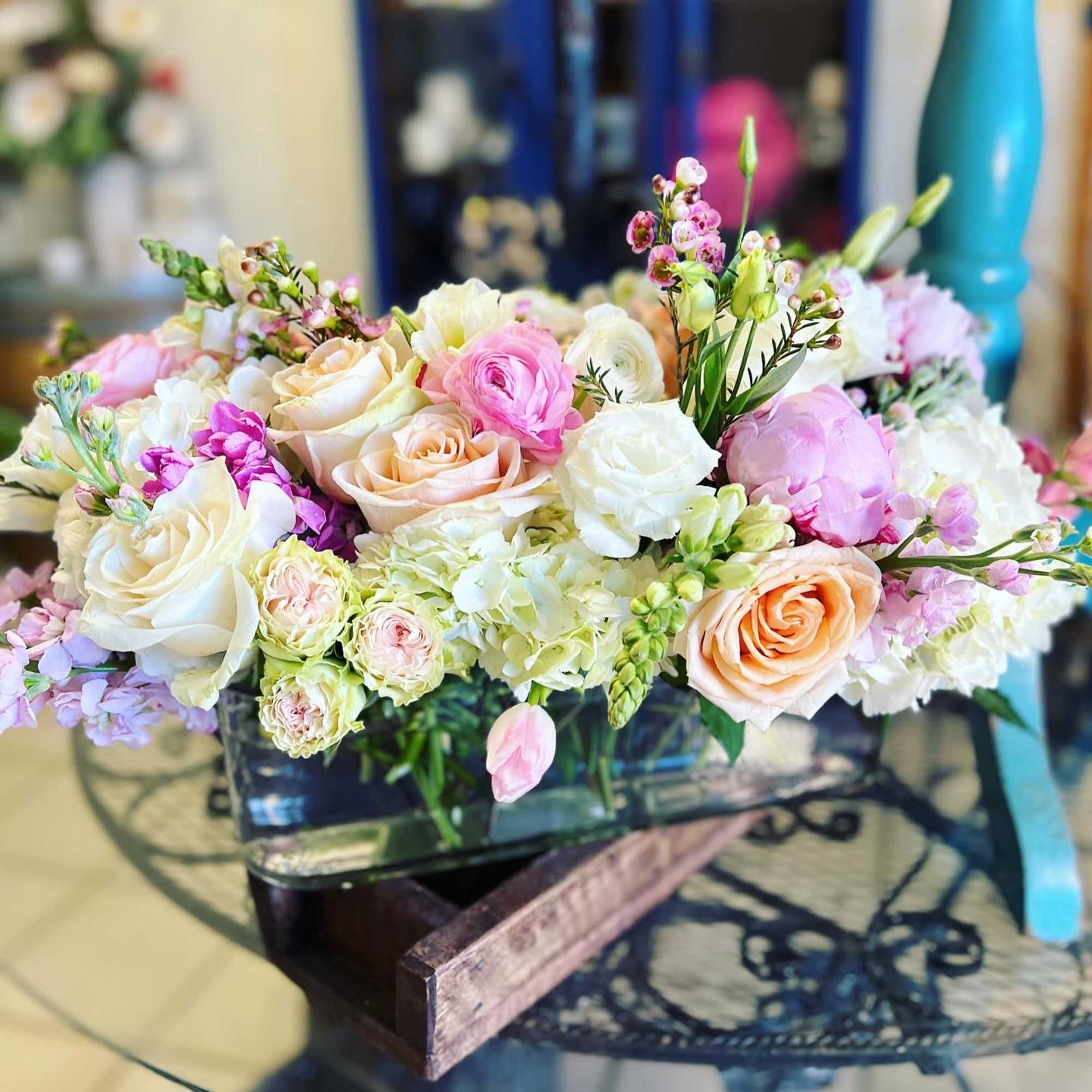 Low floral arrangement of pink, peach, and white blooms in a glass container
