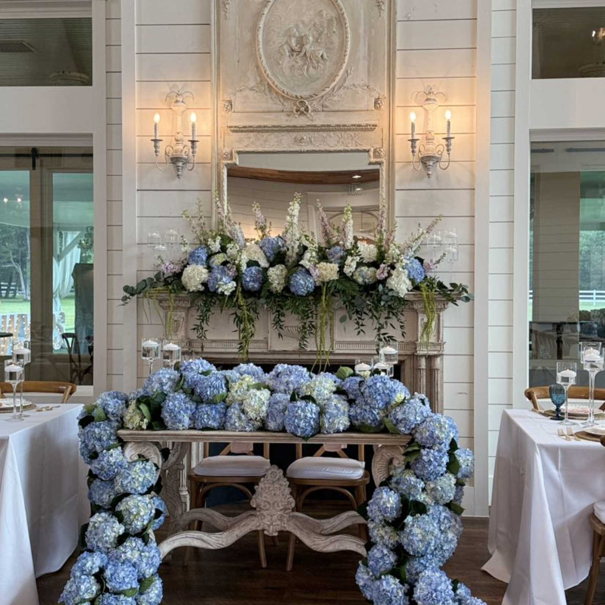 Blue and white floral arrangements on a mantel and table in a formal room