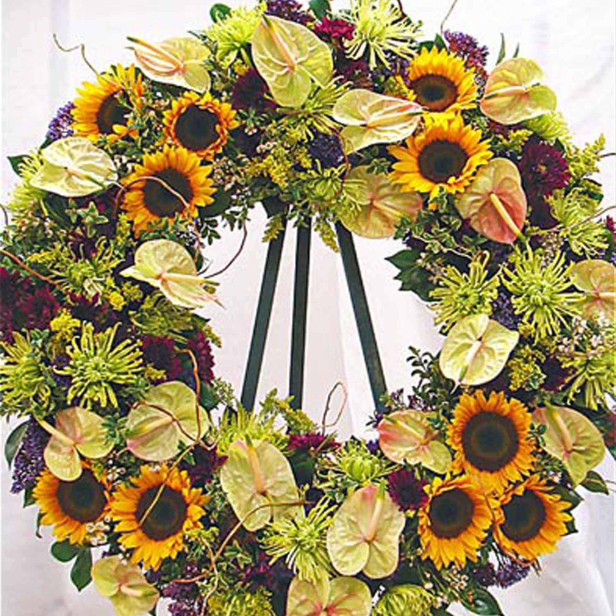 Standing wreath of sunflowers, green mums, and pale anthuriums on a metal easel.