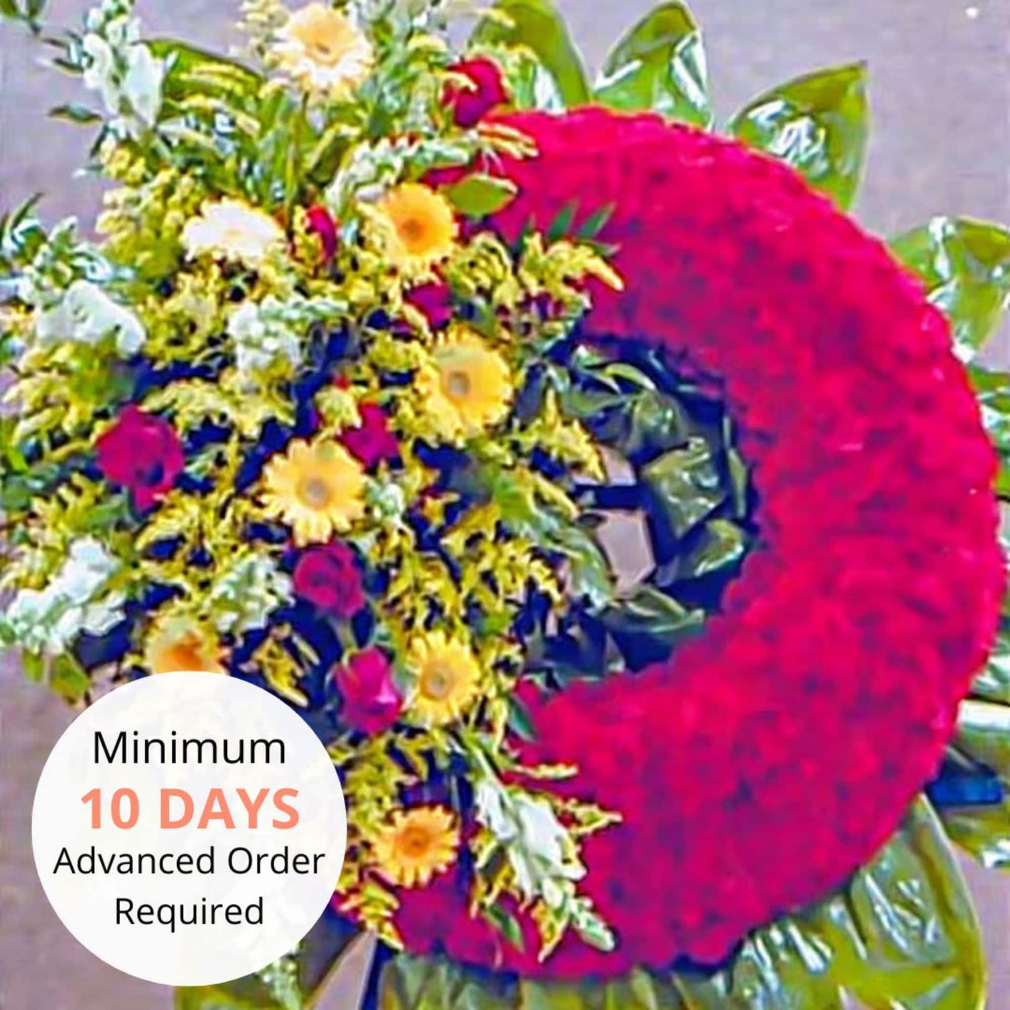 Standing red wreath with yellow and white flower cluster on one side on a wreath stand.