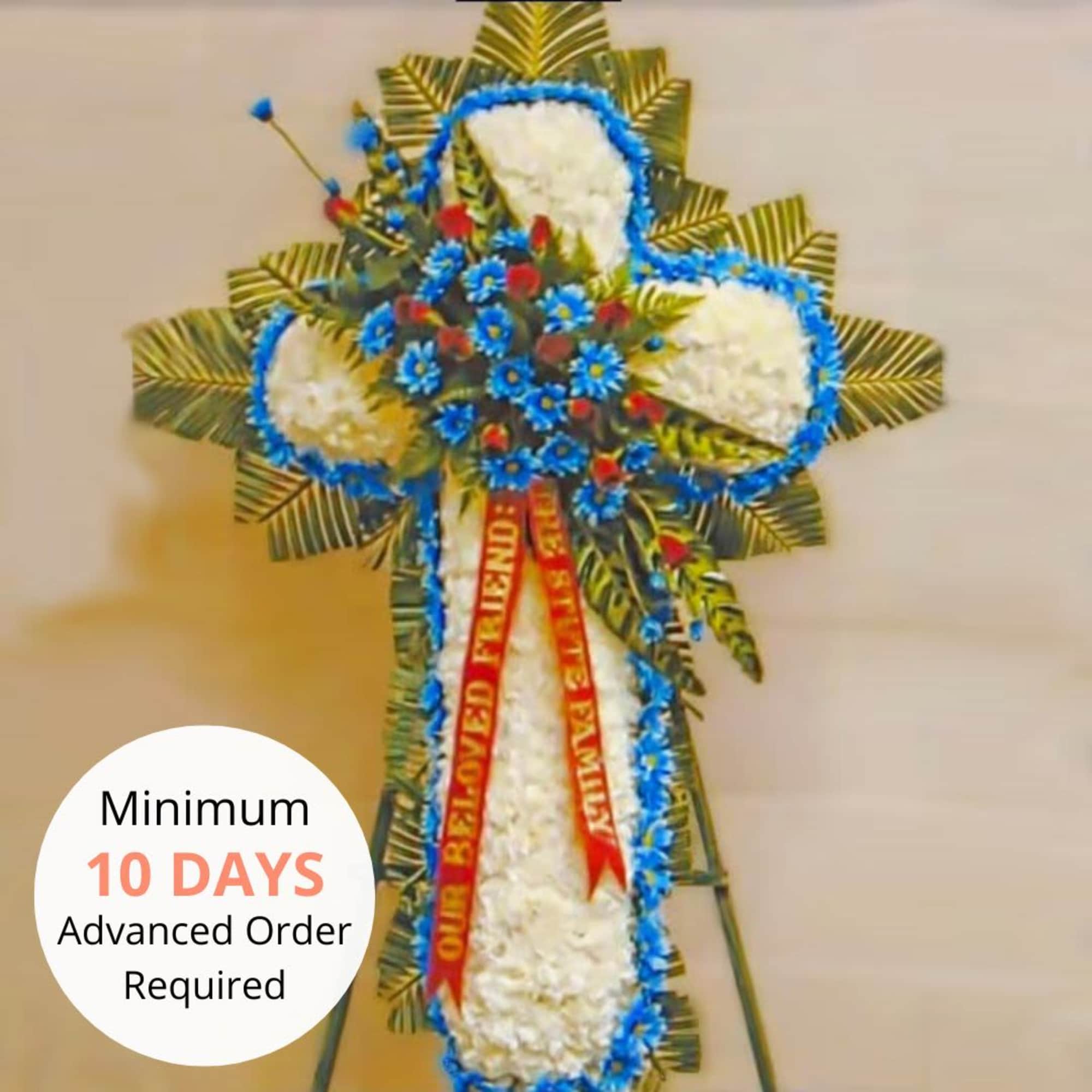 Standing white floral cross with blue and red flowers and memorial ribbon on an easel.