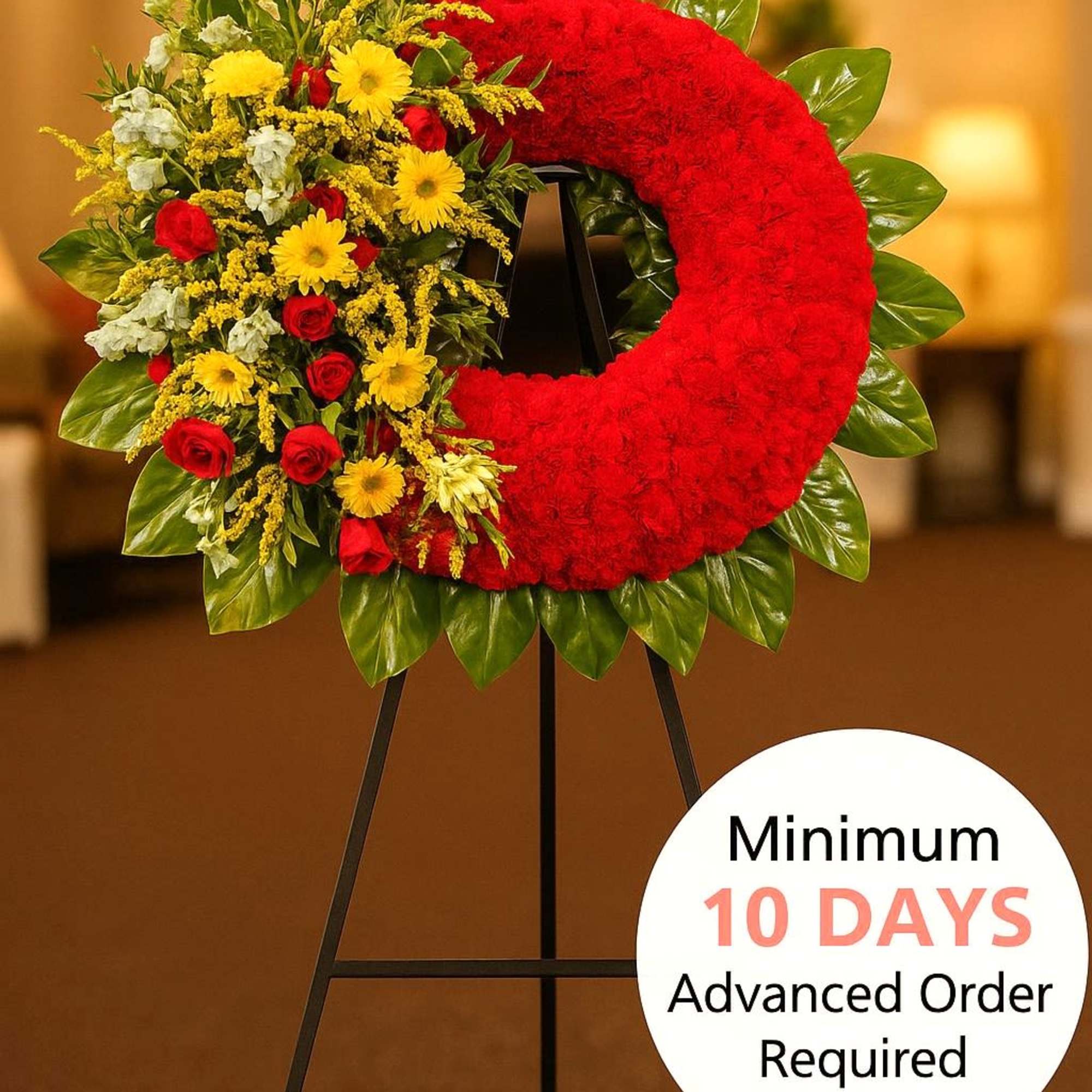 Standing red wreath with yellow and red flowers on one side, displayed on a black easel indoors