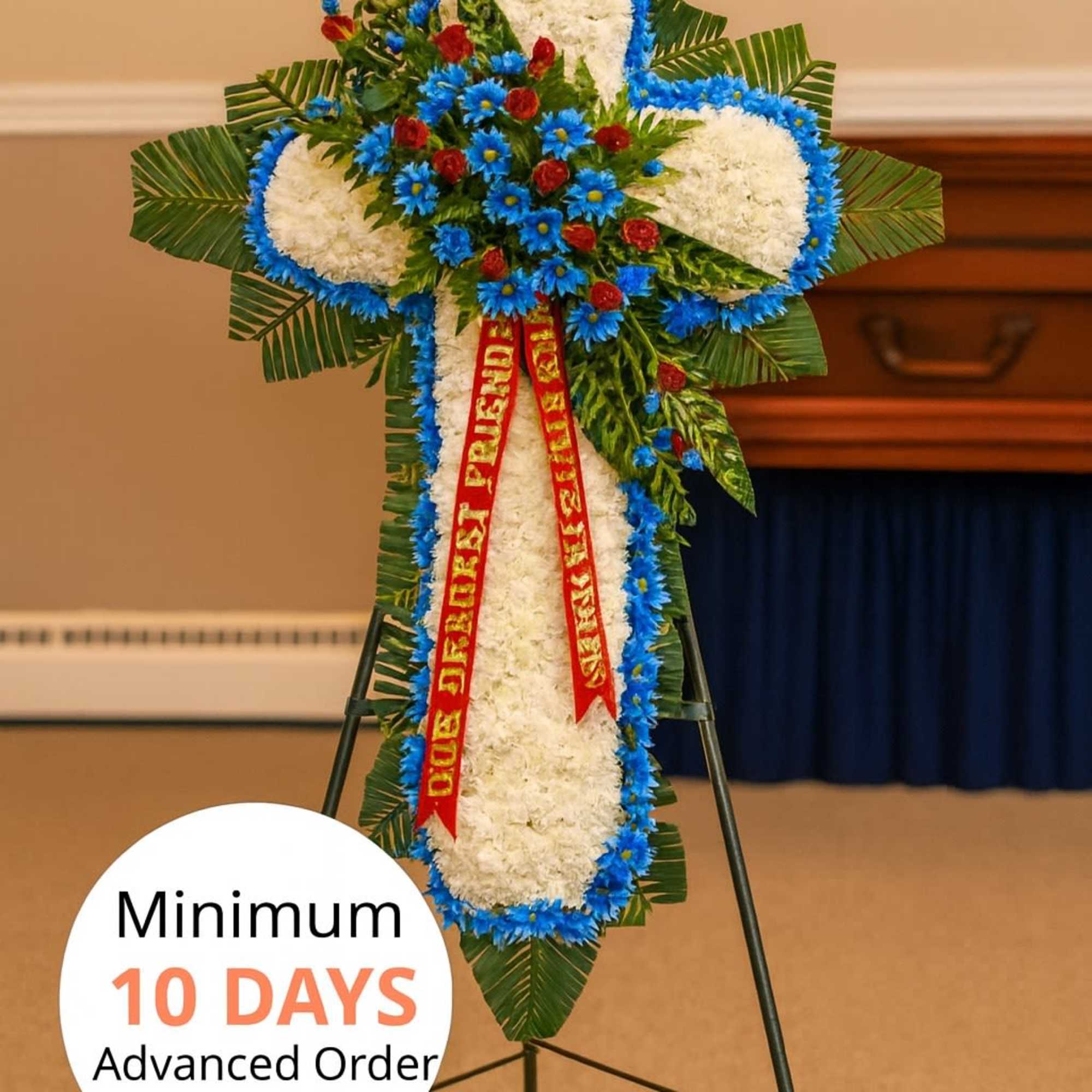Standing cross-shaped funeral spray of white flowers with blue and red accents on an easel