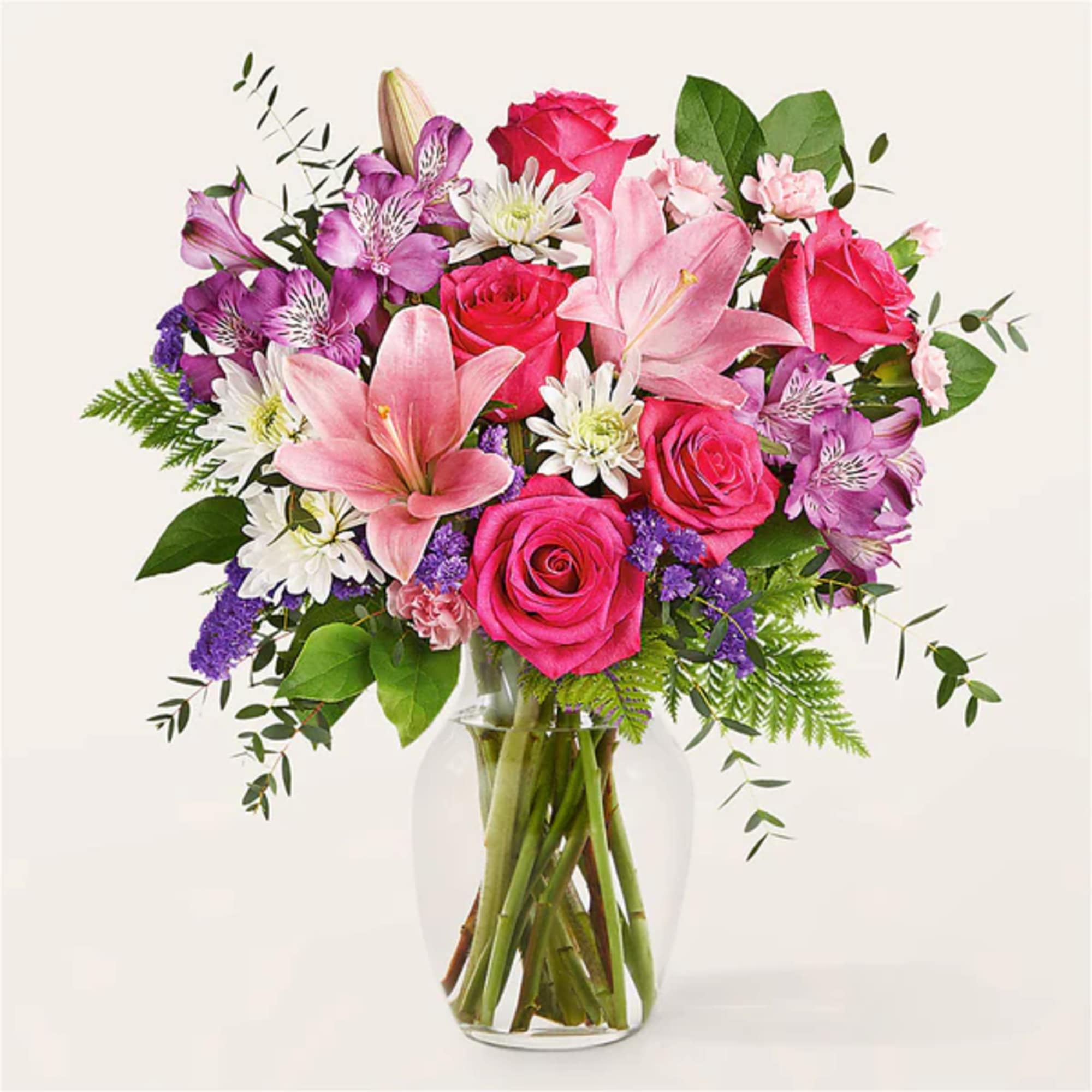 Bouquet of pink roses, lilies, and purple flowers in a clear glass vase