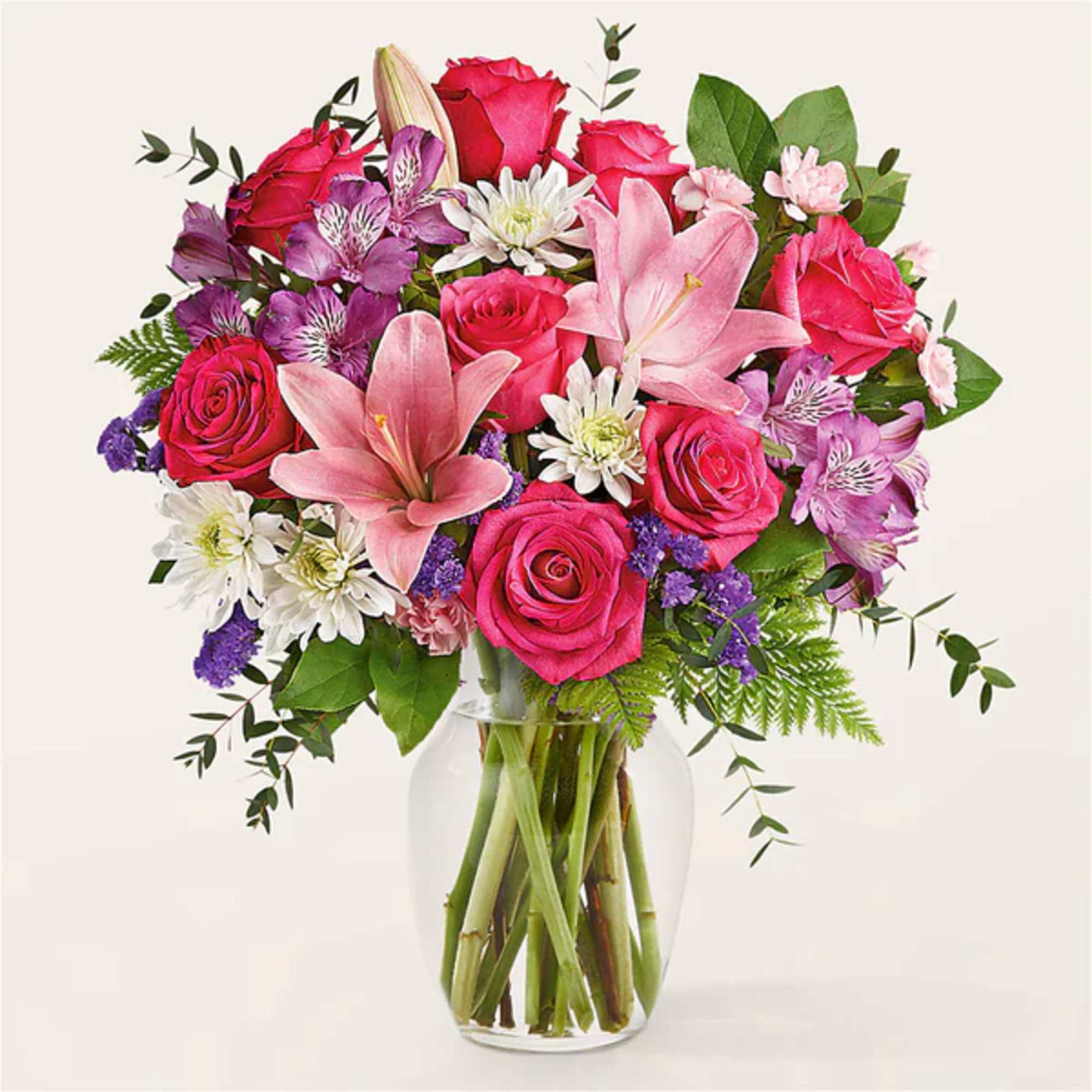 Bouquet of pink roses, lilies, and purple flowers in a clear glass vase