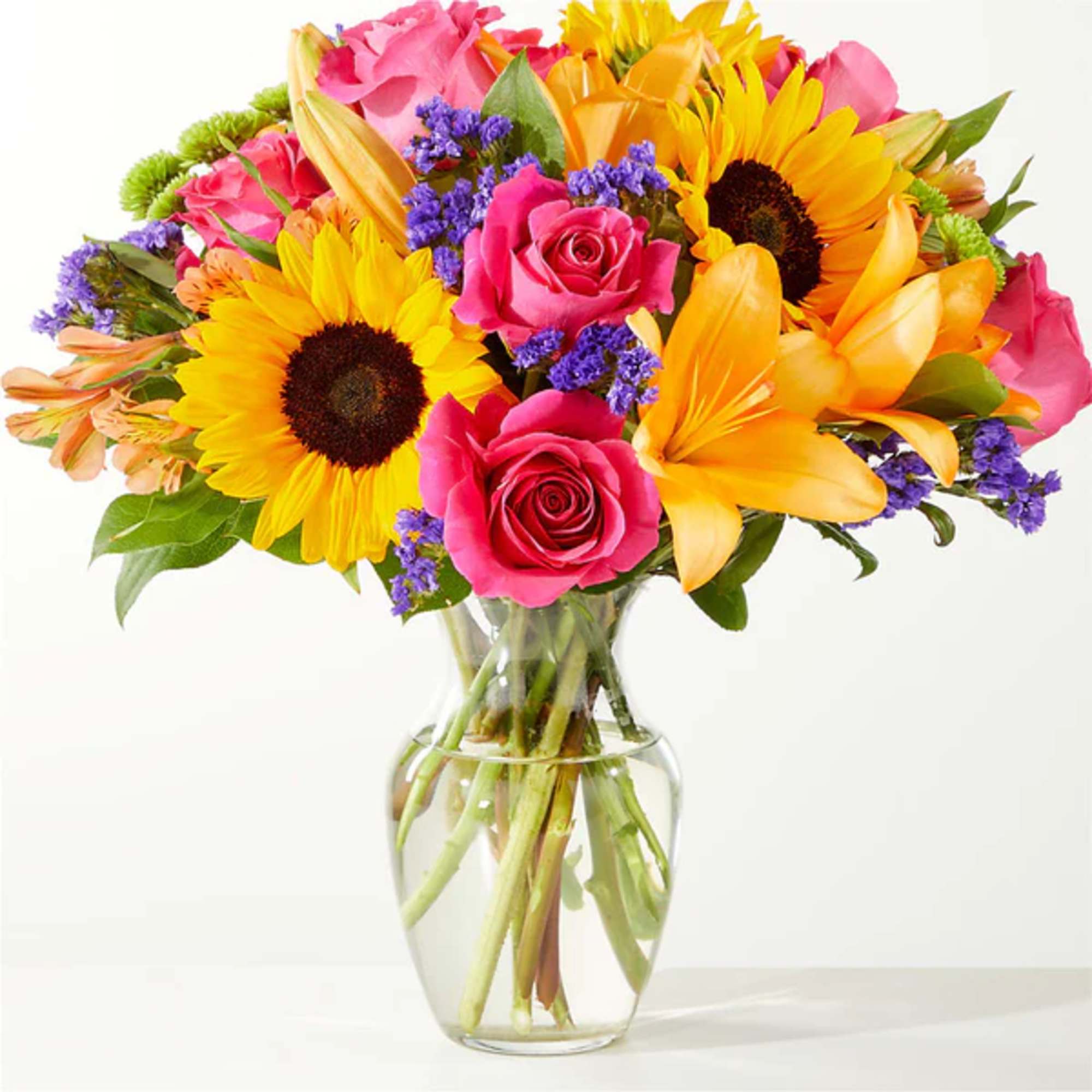 Bouquet of sunflowers, pink roses, and yellow lilies in a glass vase