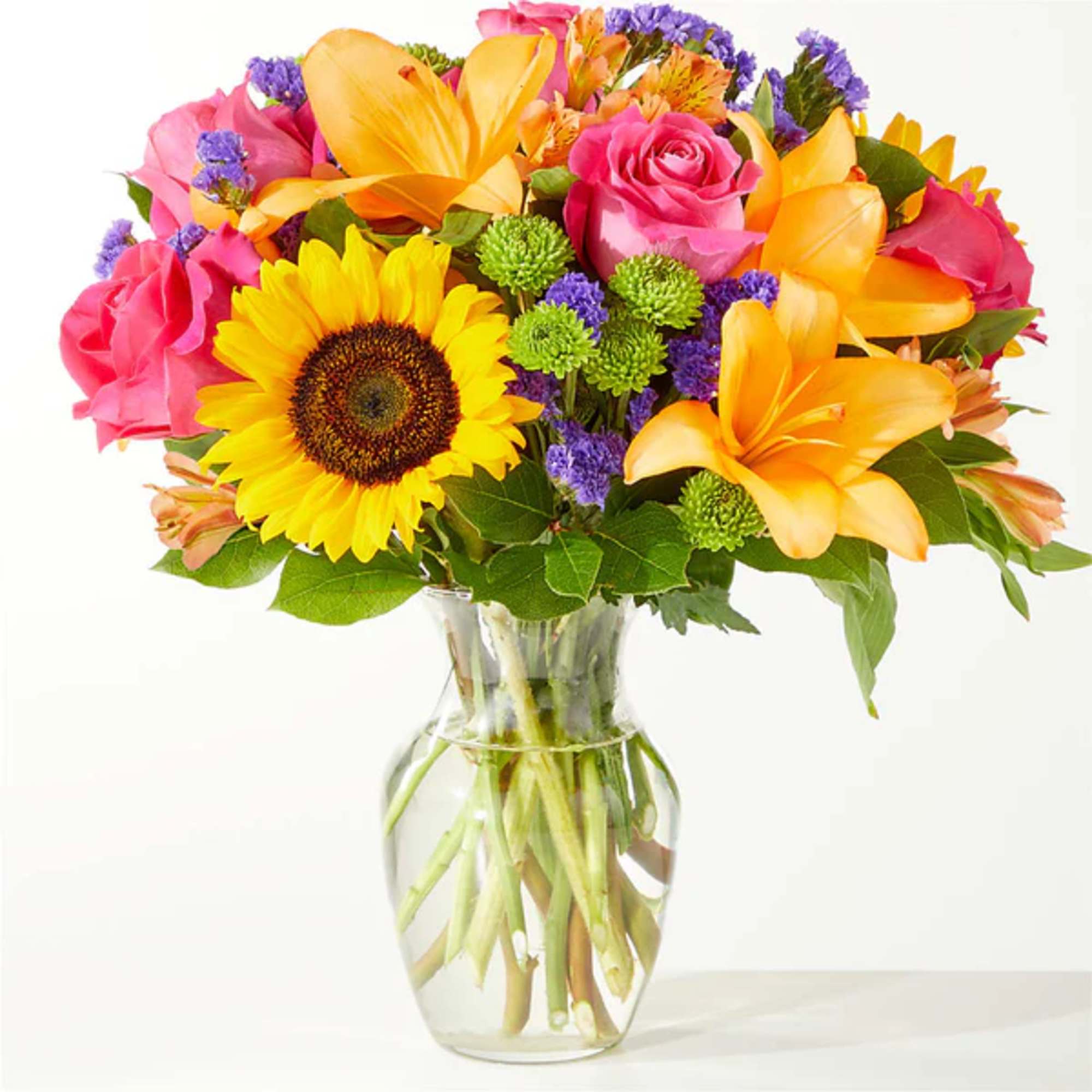 Colorful bouquet of sunflowers, roses, and lilies in a clear glass vase