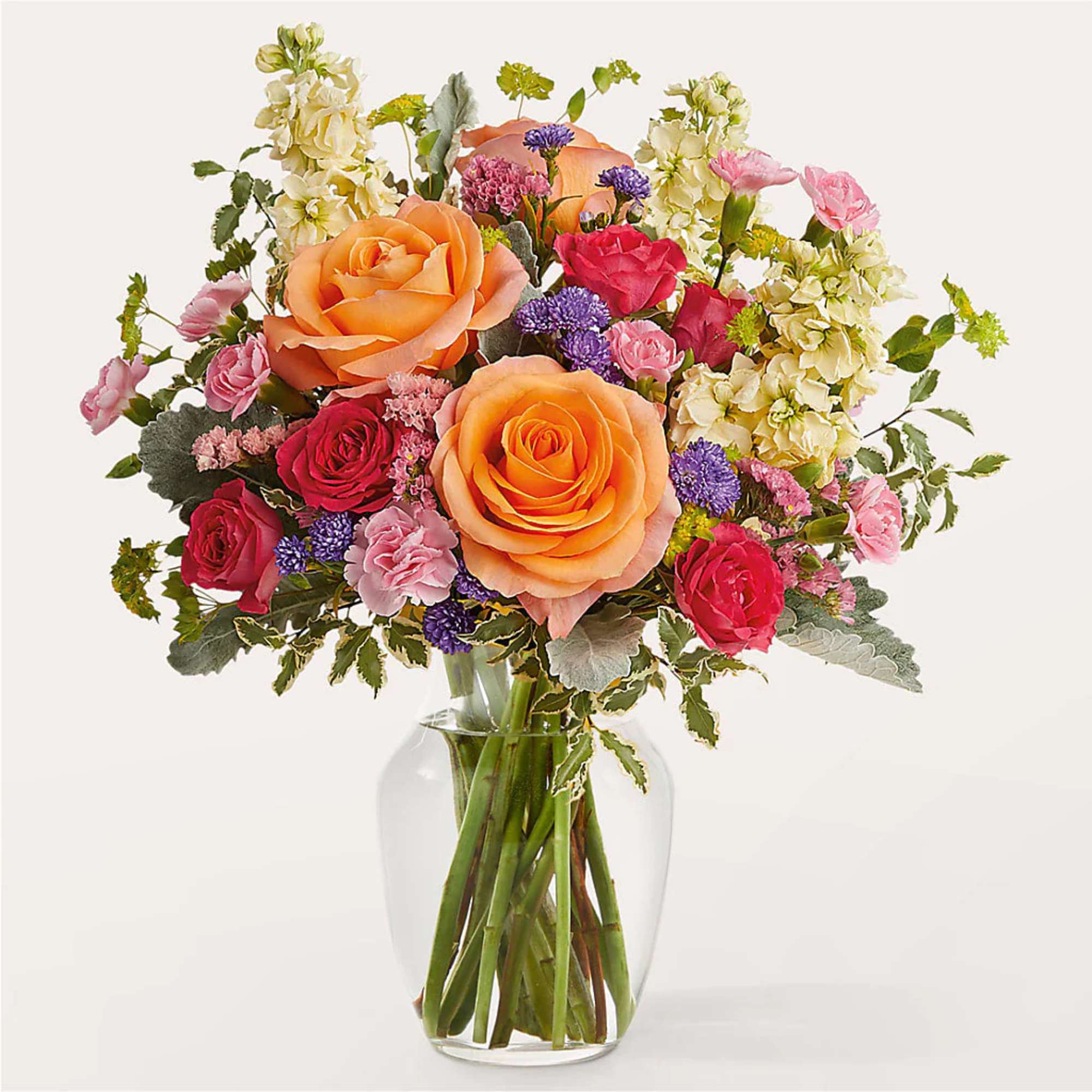 Mixed bouquet of roses, carnations, and purple filler flowers in a clear glass vase