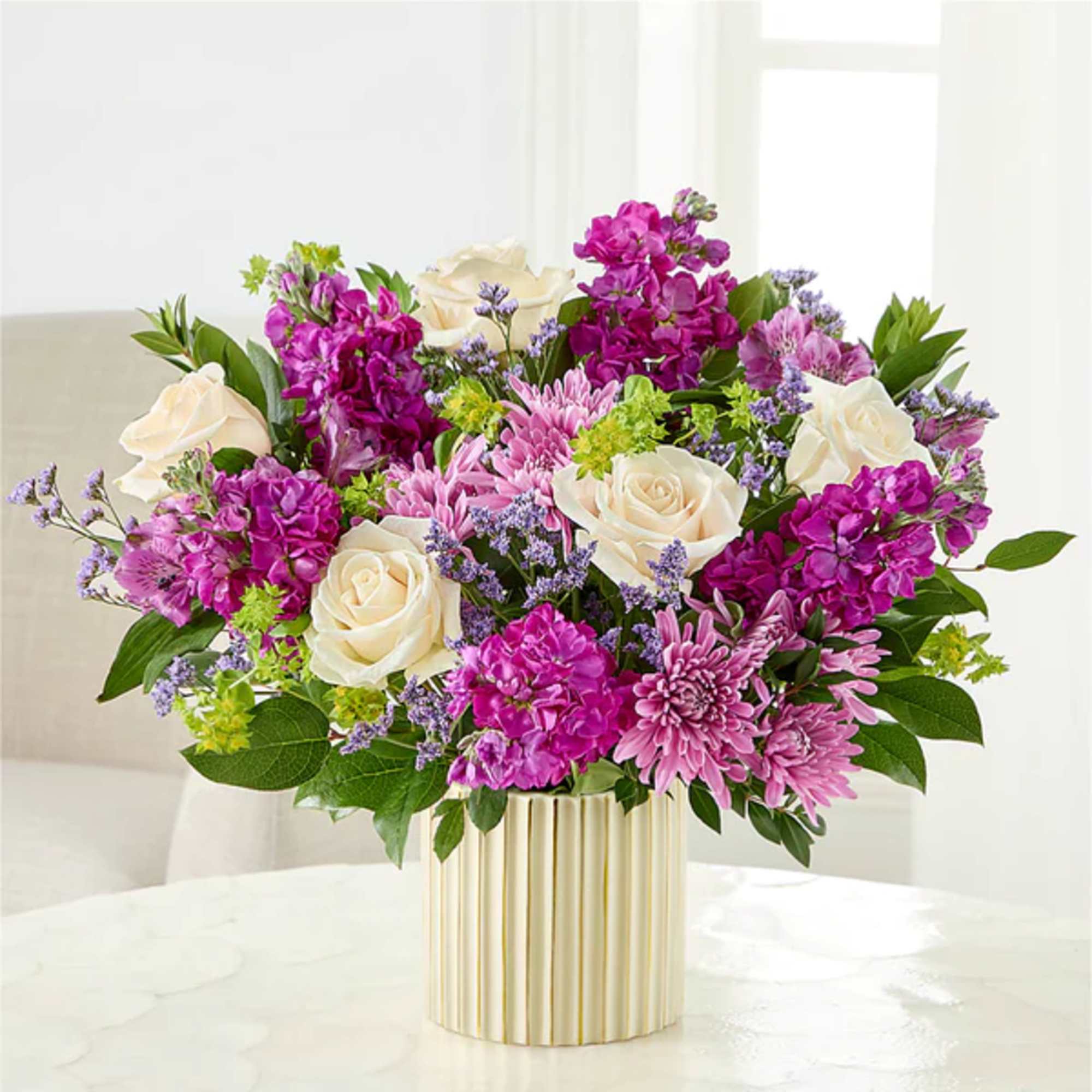 Bouquet of white roses, pink flowers, and purple blooms in a striped vase