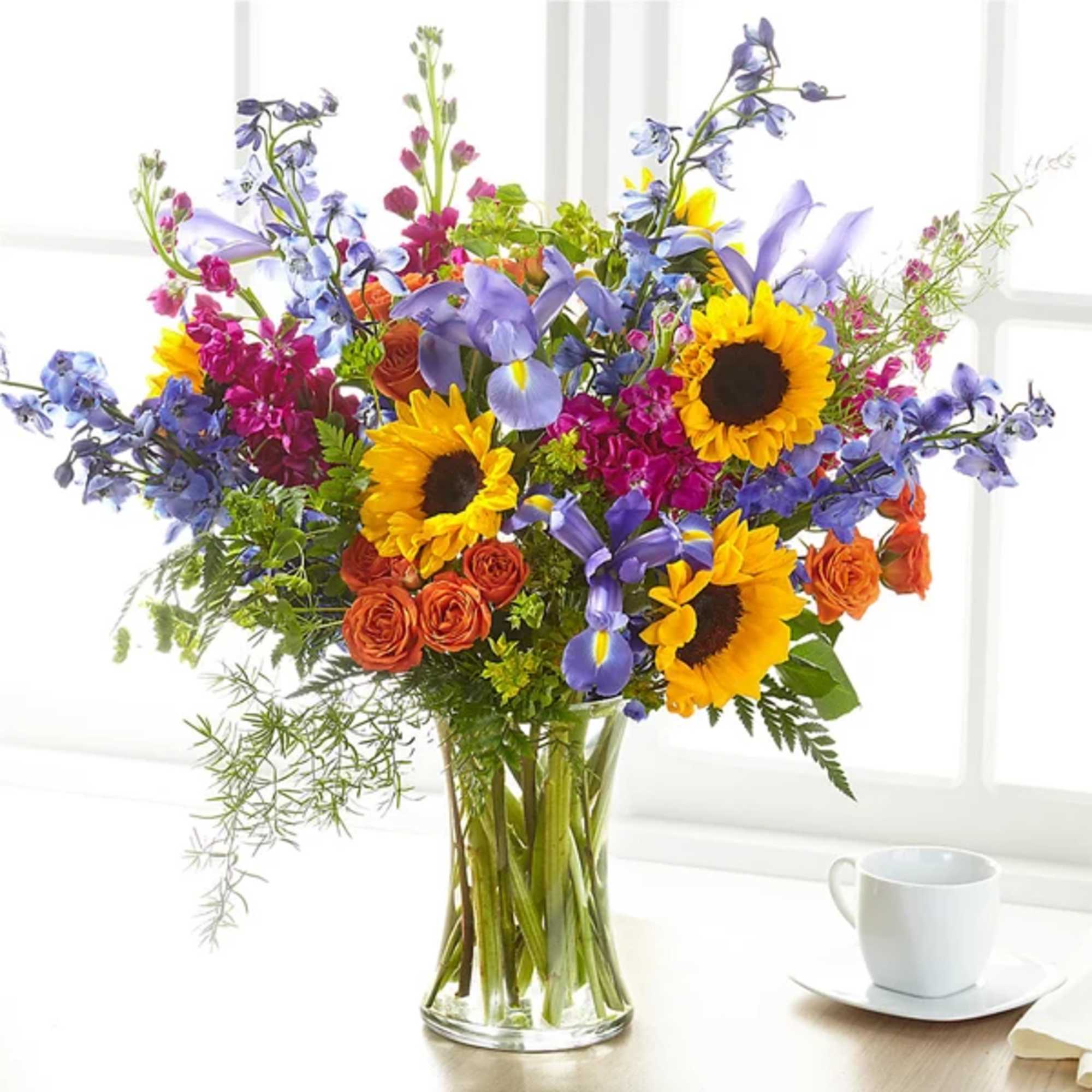 Colorful bouquet with sunflowers, irises, and orange roses in a clear glass vase