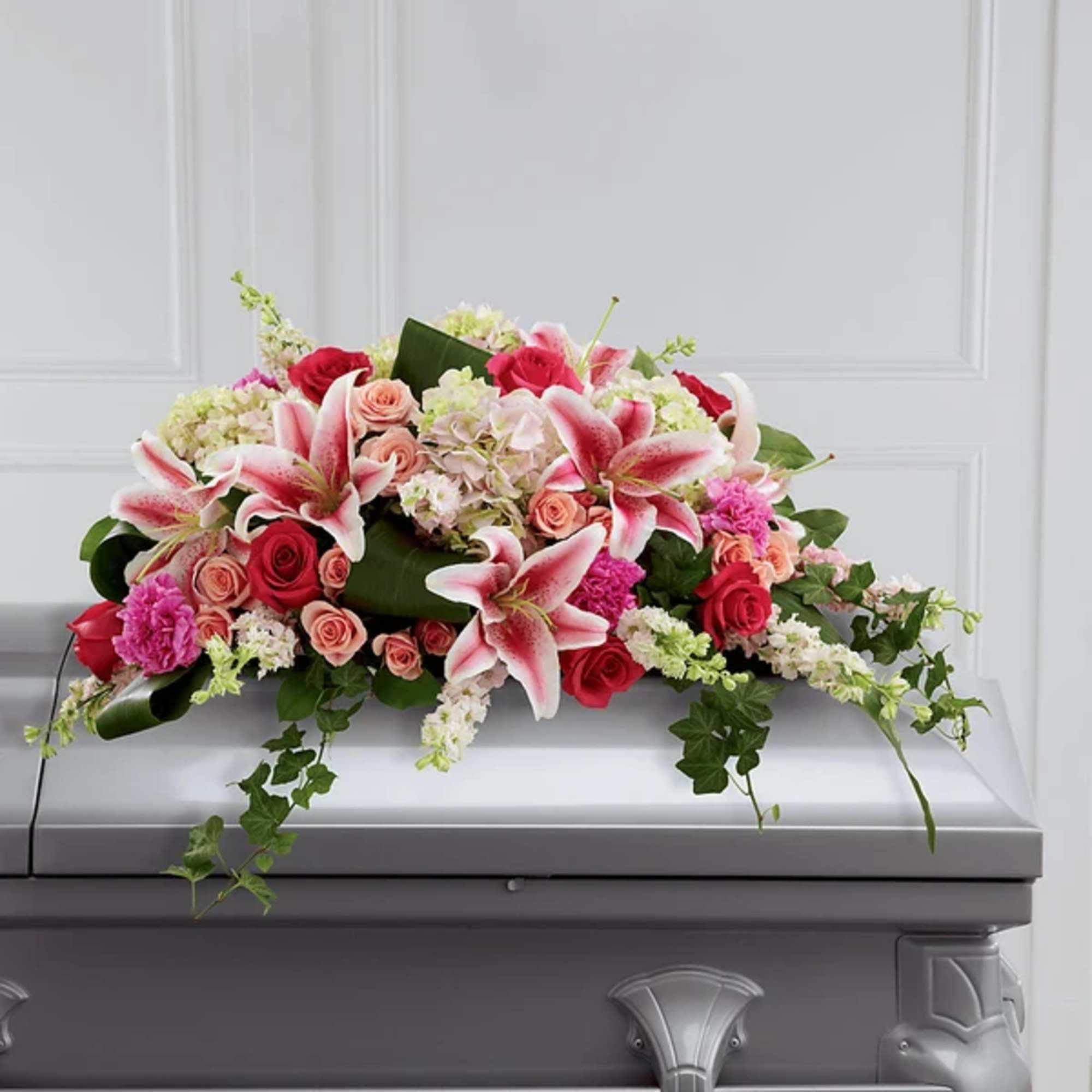 Casket spray with pink lilies, roses, and mixed blooms