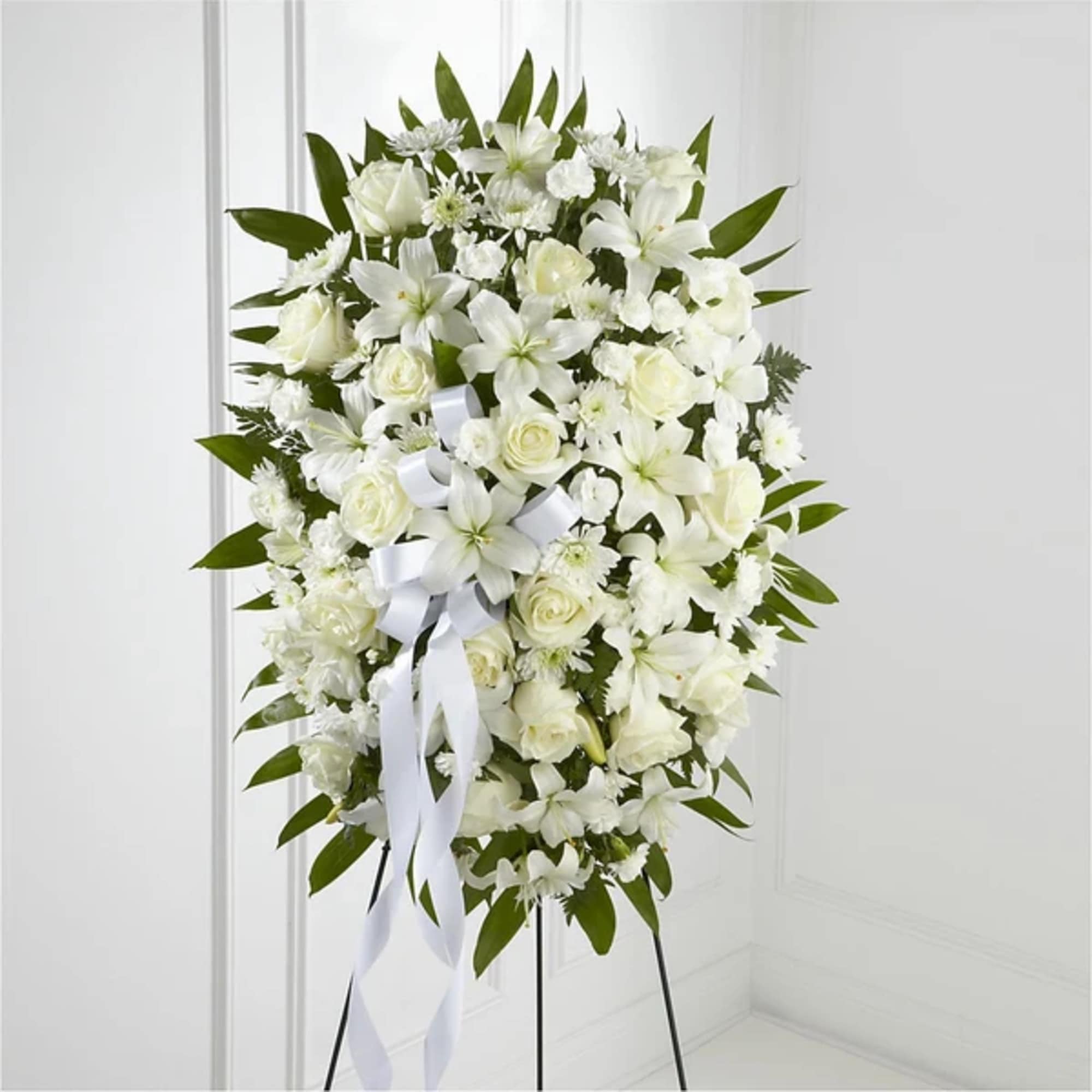 White funeral spray of roses and lilies on a stand with a white ribbon
