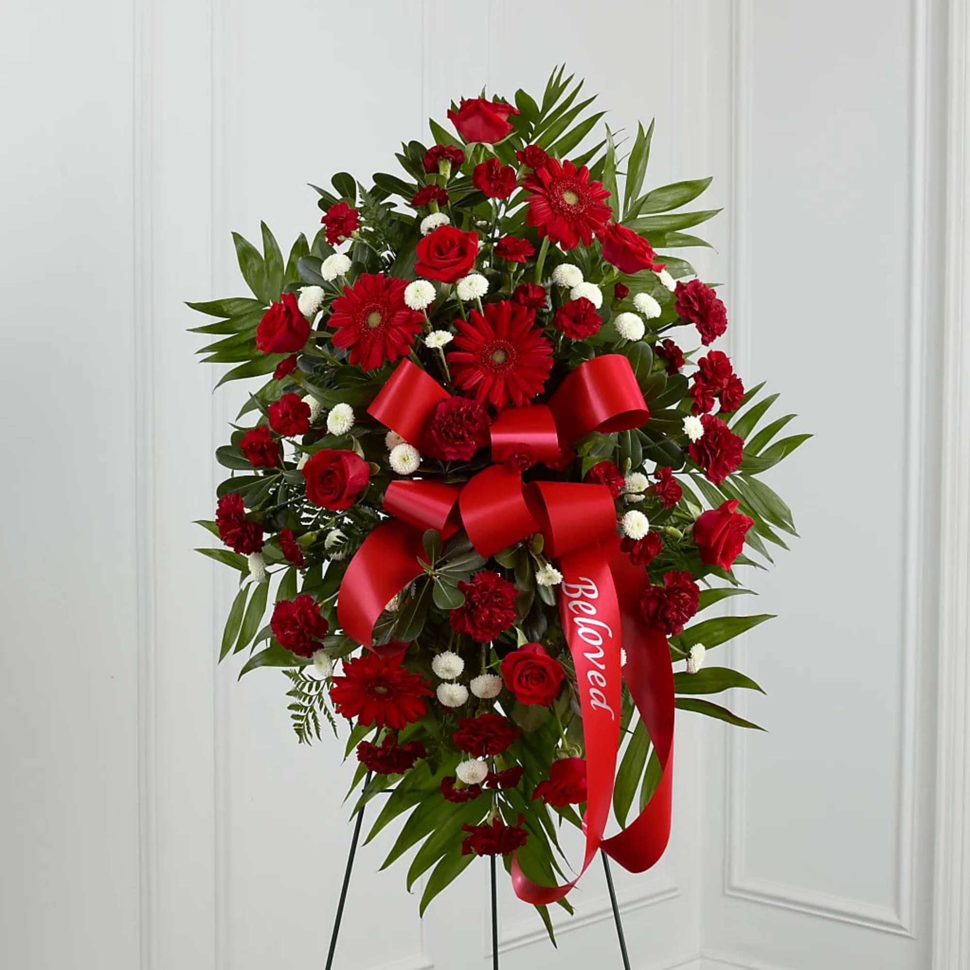 Red floral standing spray with a large red ribbon on a black easel
