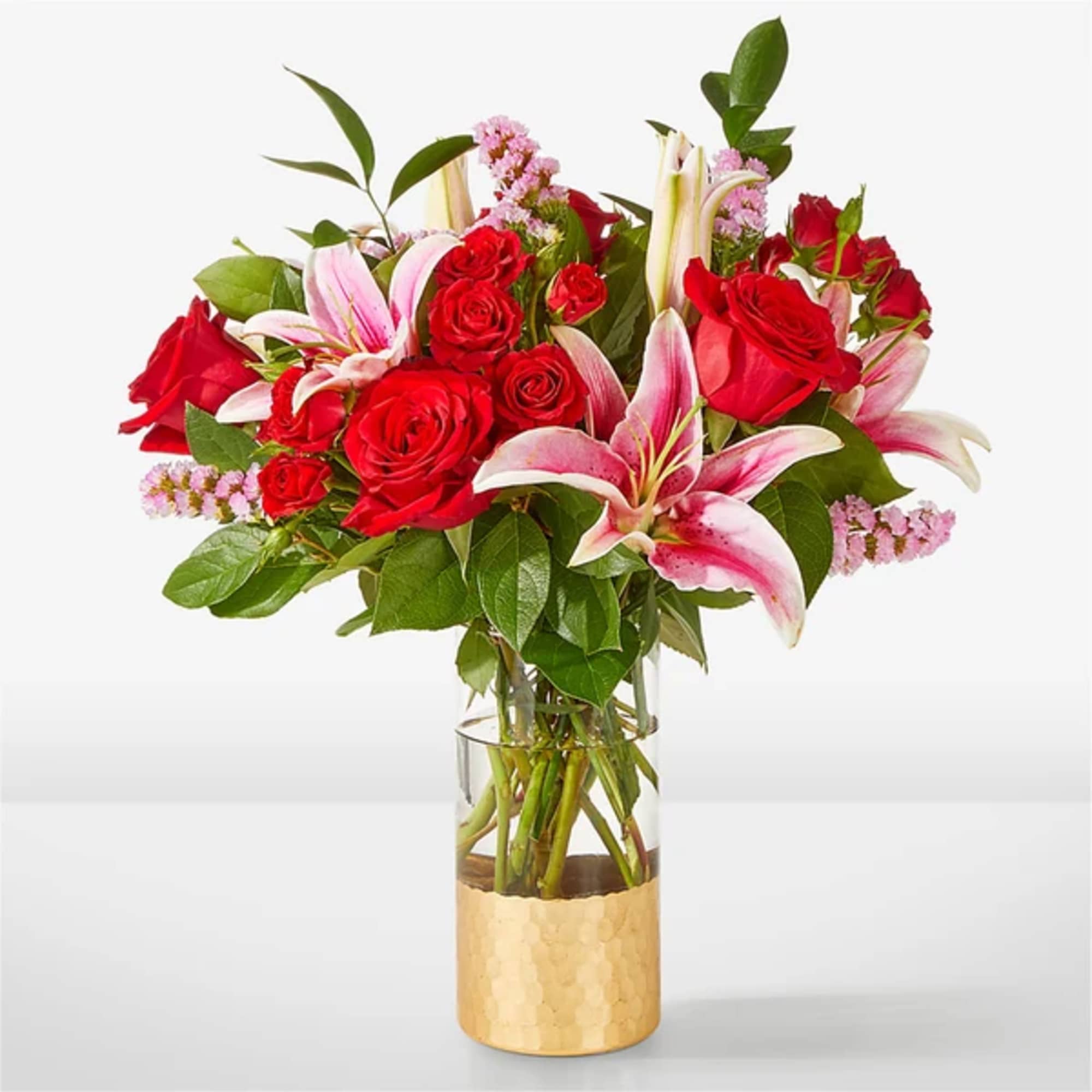 Red roses and pink lilies in a clear vase with a gold base