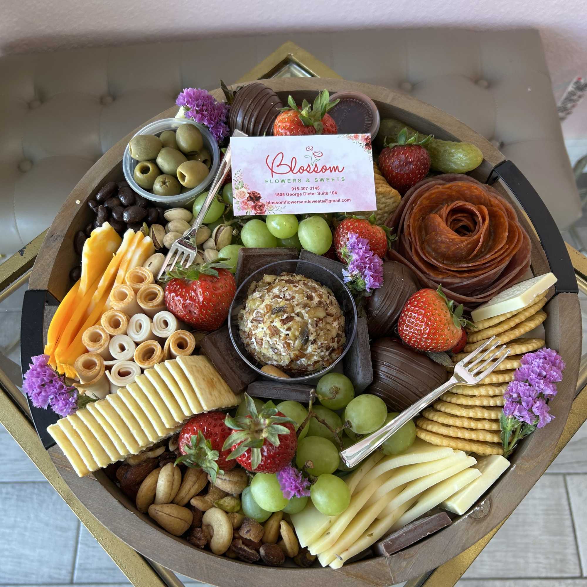 Charcuterie gift tray with fruit, cheese, crackers, nuts, and small purple flowers