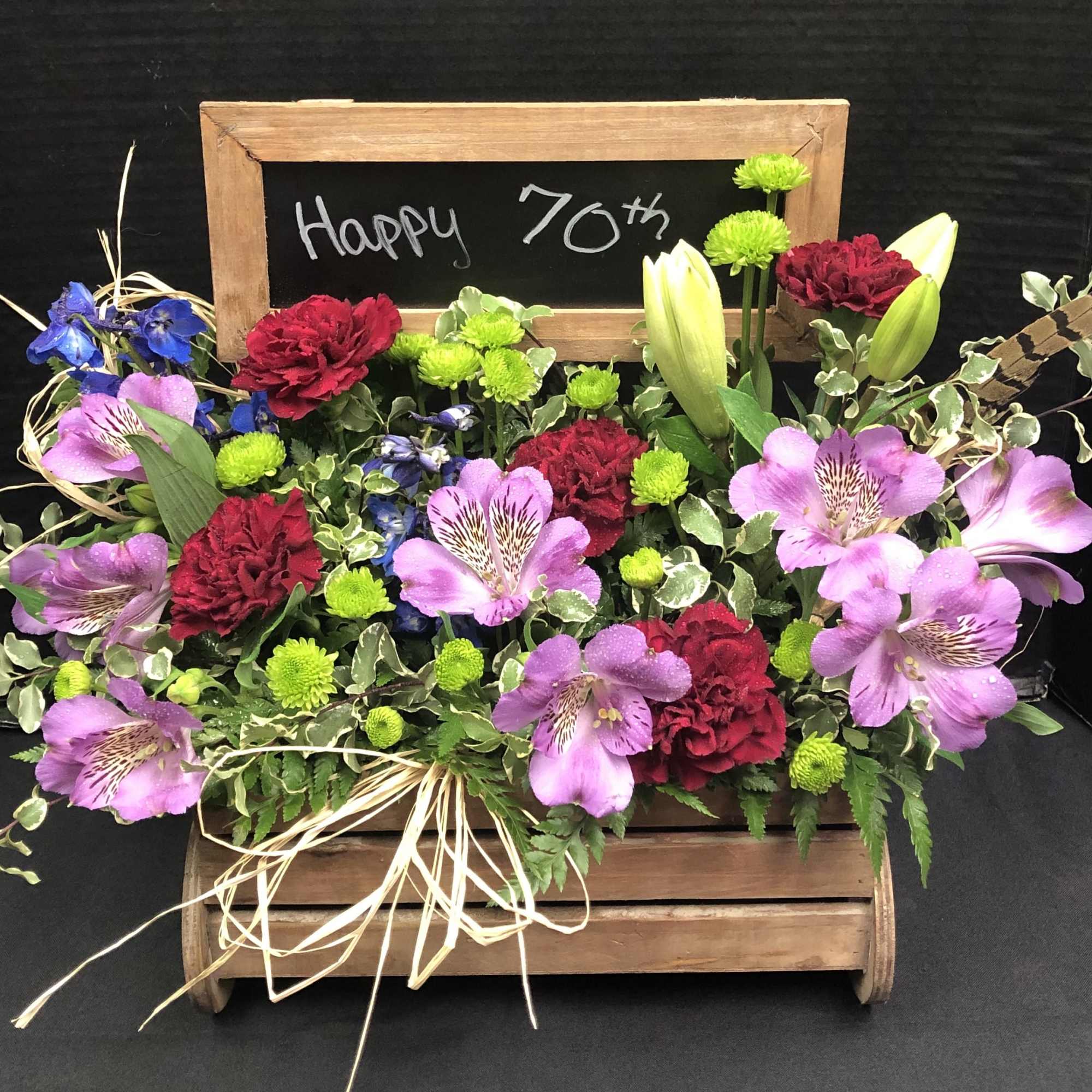 Mixed flower arrangement in a wooden crate with a "Happy 70th" chalkboard sign